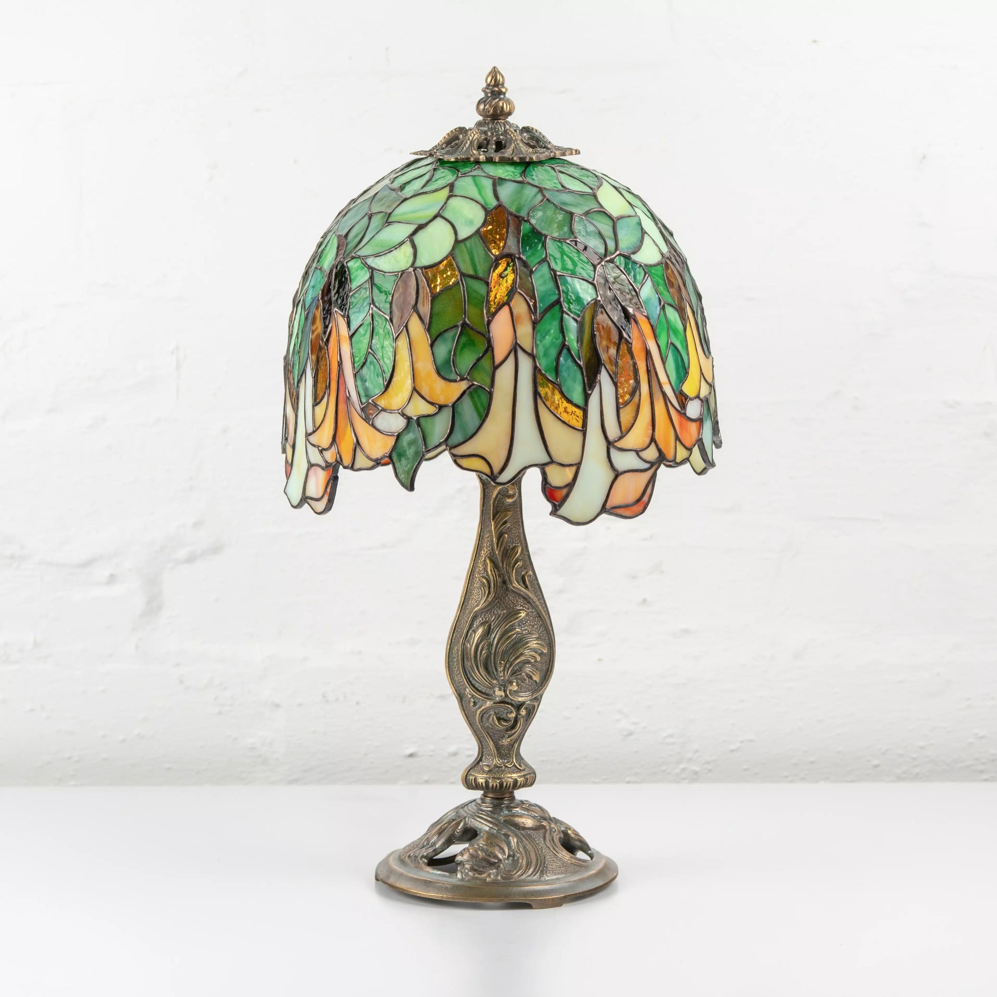 Full view of Art Nouveau stained glass table lamp with green and yellow floral dome and detailed bronze base.