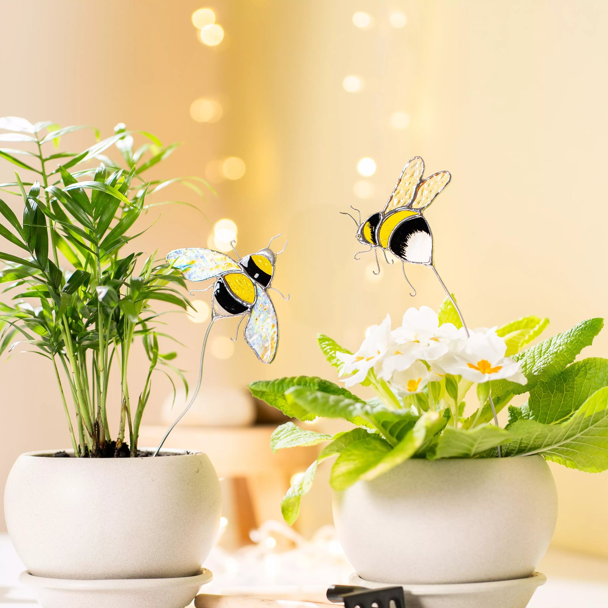 Two stained glass bee plant stakes in plant pots with a warm, blurred background