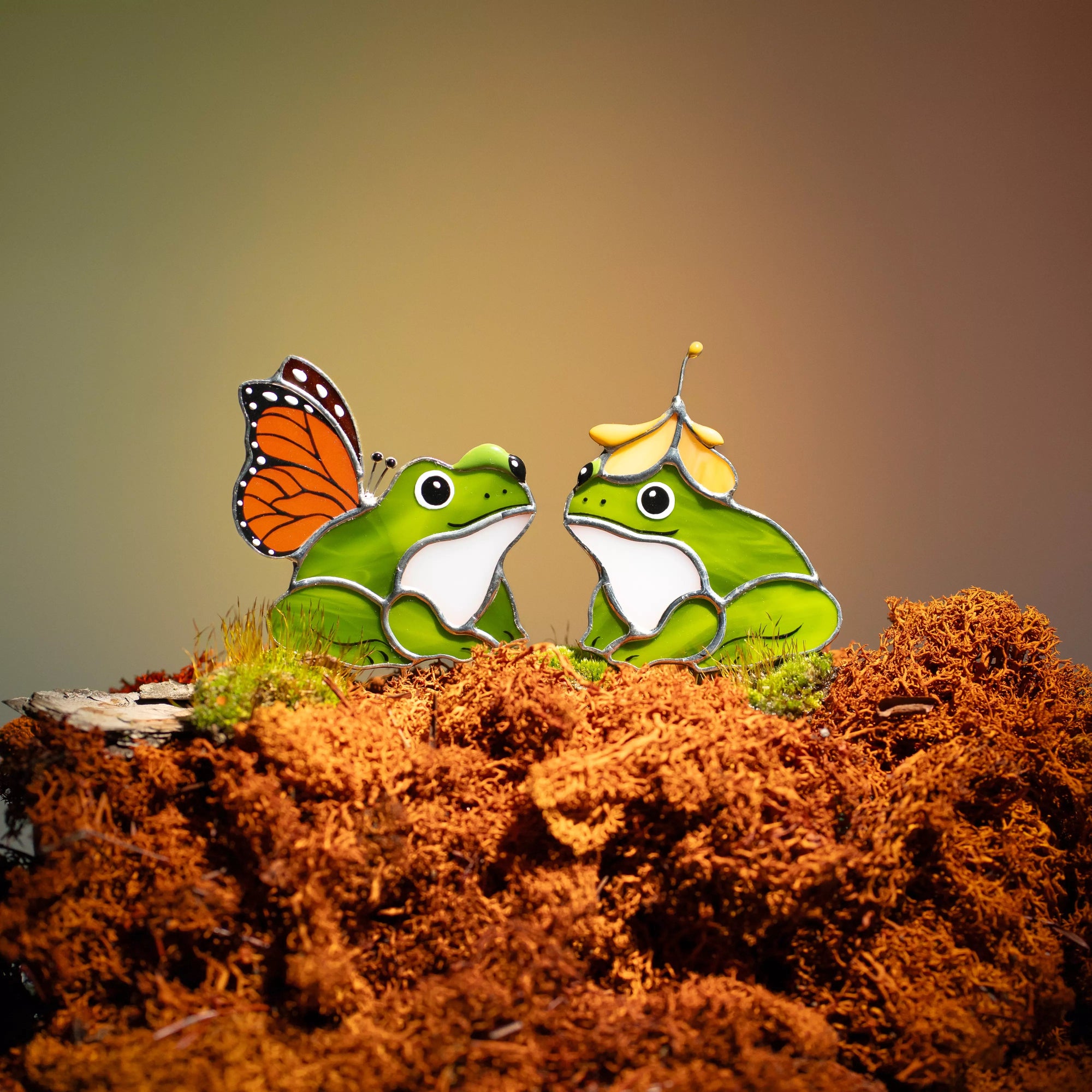 Two stained glass green frogs with a butterfly on a brown surface