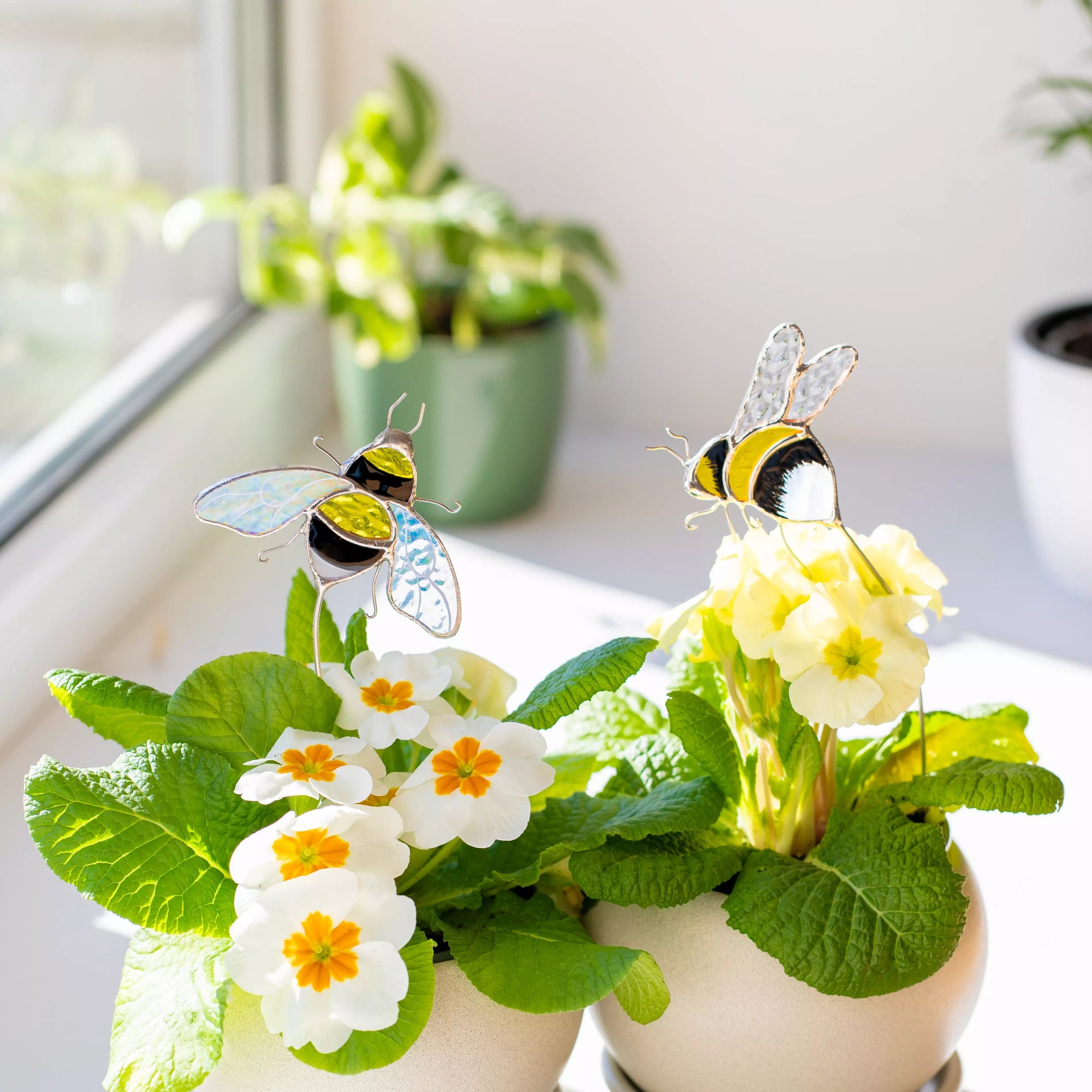 Two small potted plants with decorative stained glass plant stakes bees on a windowsill.