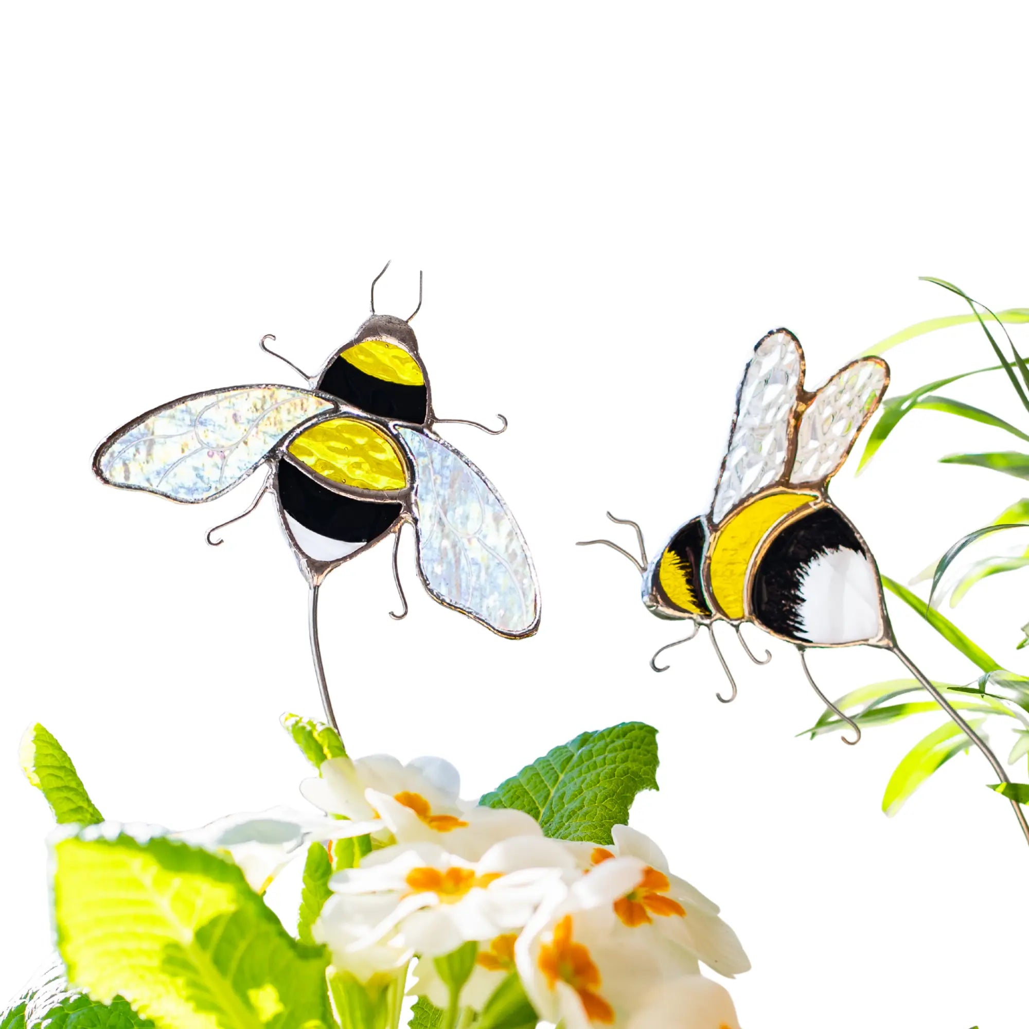 Two stained glass bee plant stakes on a white background with green leaves and flowers.