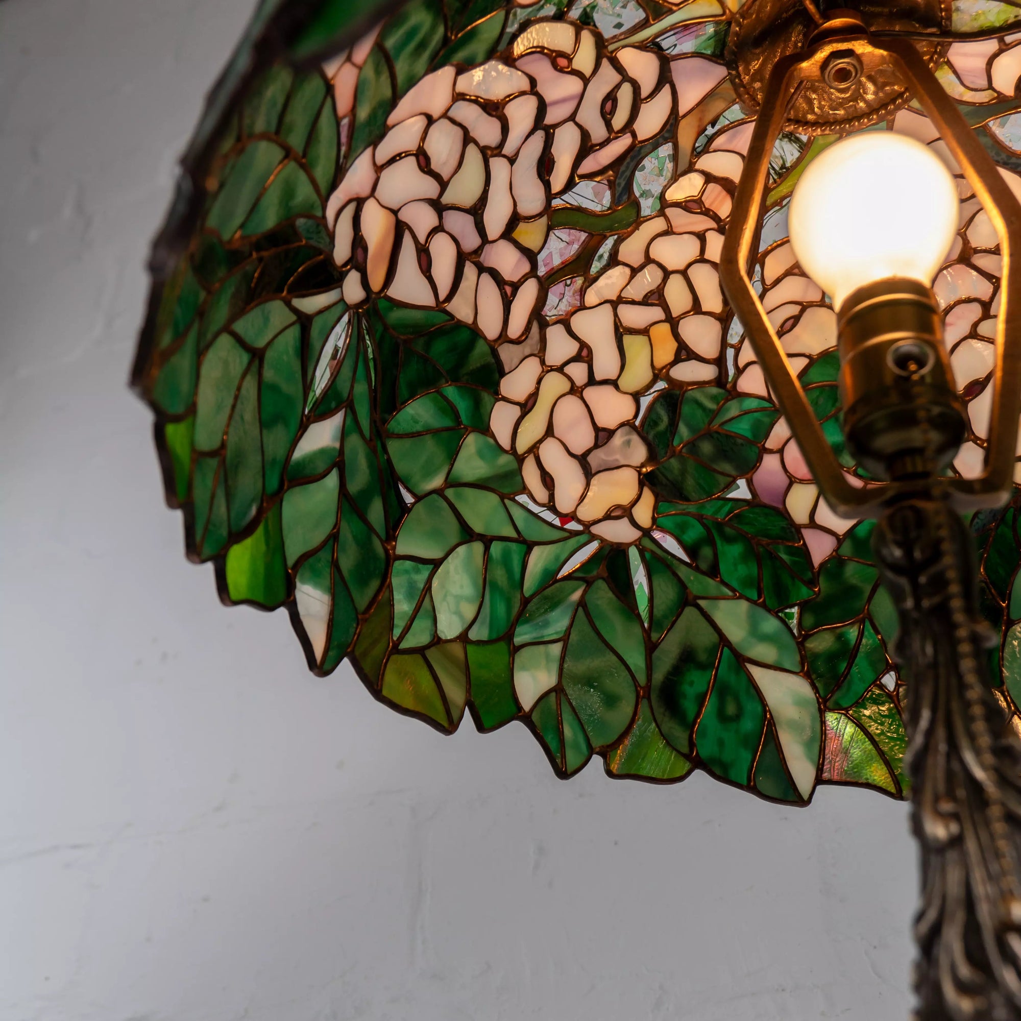 Close-up from below of stained glass lamp with blooming pink chestnut accents and green leaf design