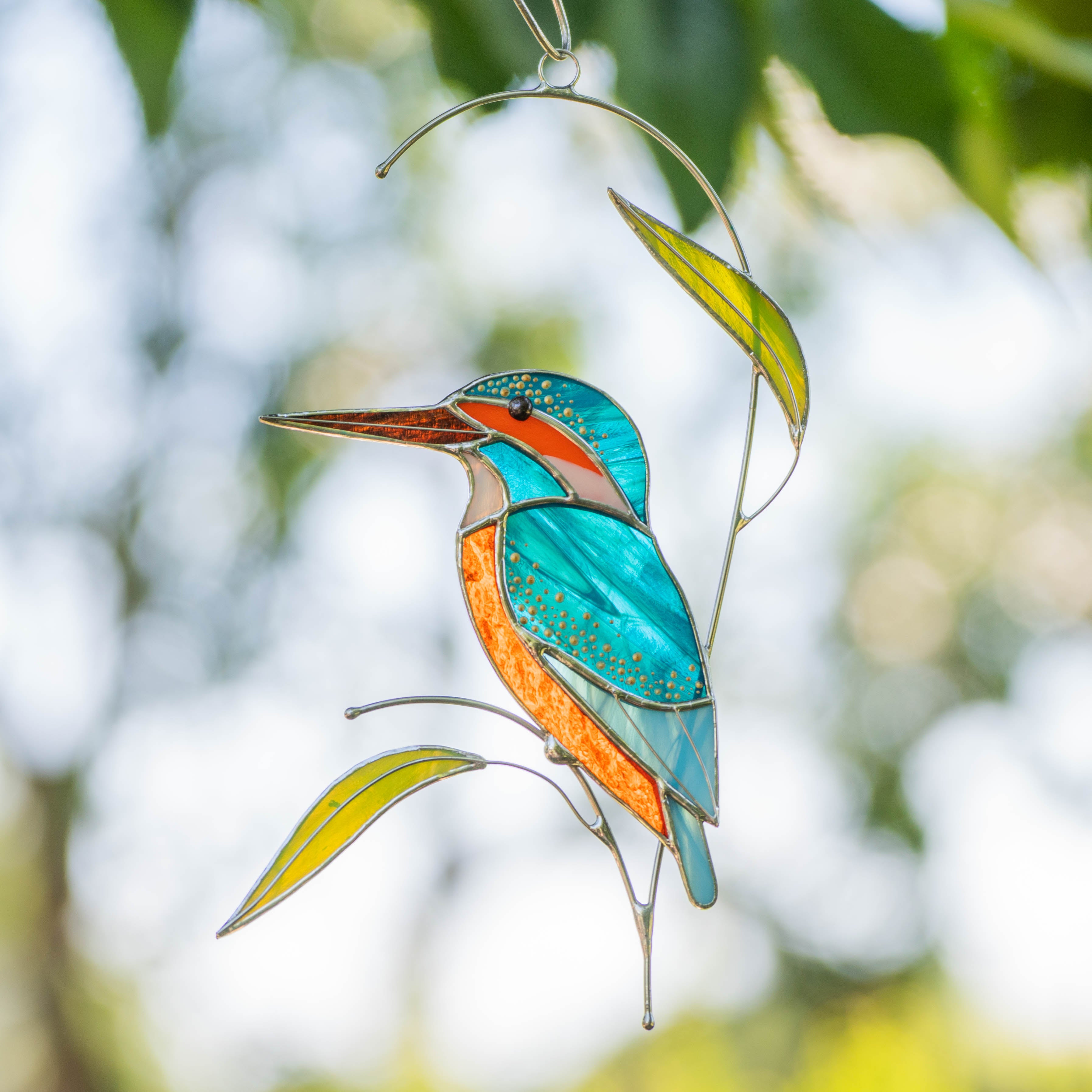 Stained glass kingfisher with bright turquoise and orange details, hanging outdoors on a sunny day.