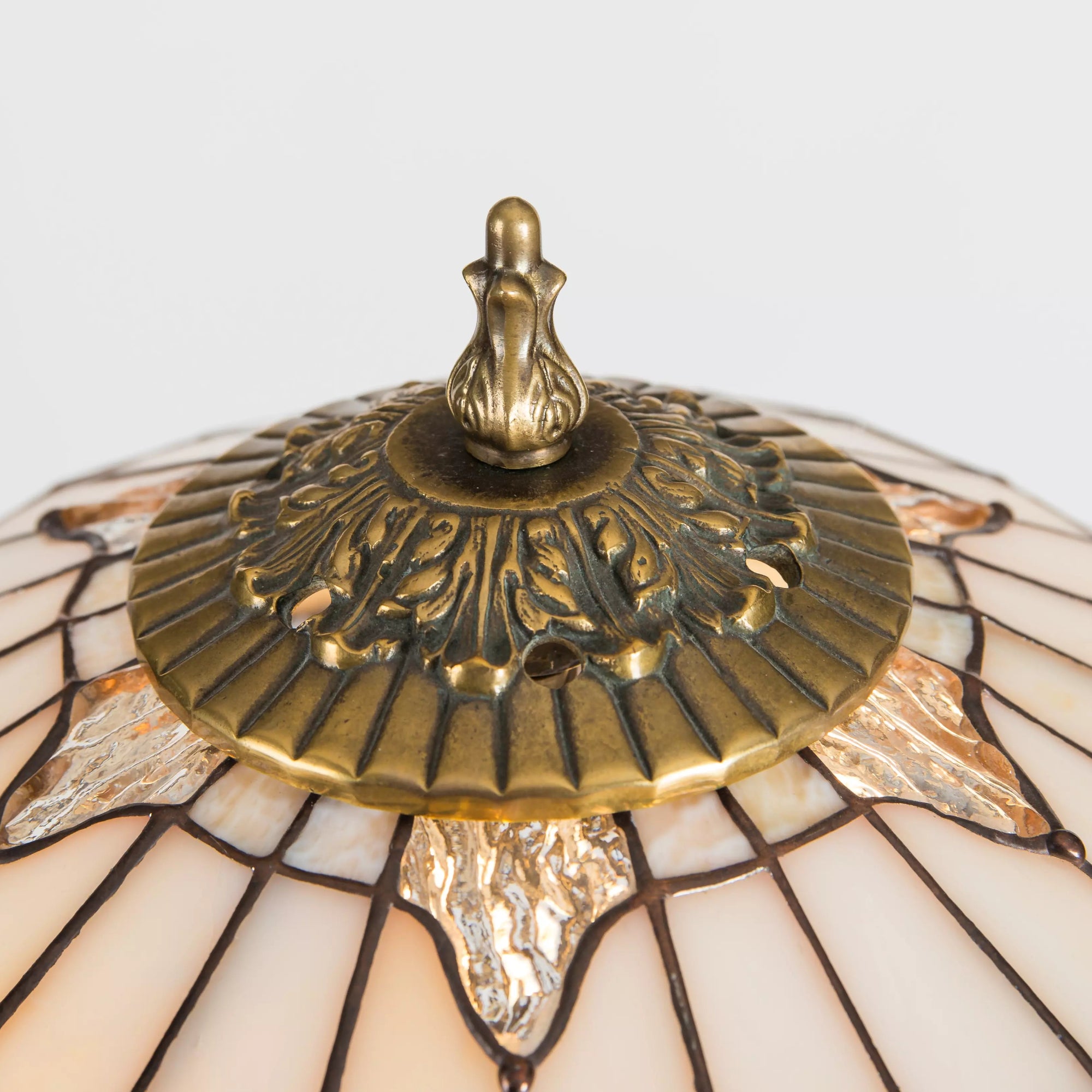 Decorative bronze finial and crown detail on top of beige stained glass lamp shade