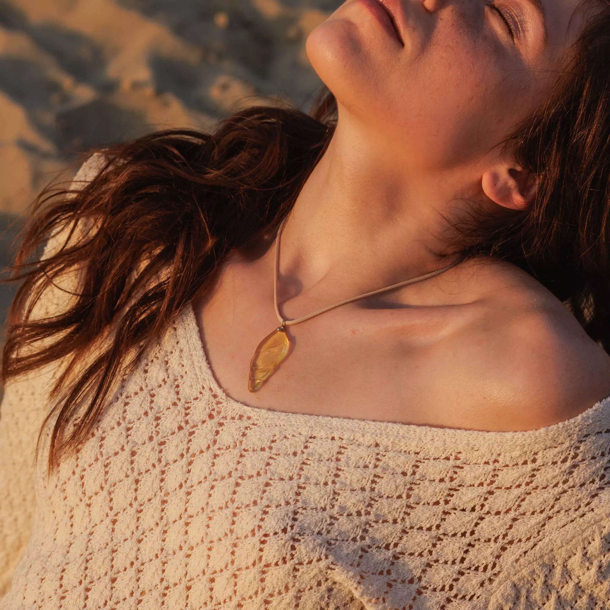 Woman wearing a necklace with a golden shell stained glass pendant against a blurred natural background