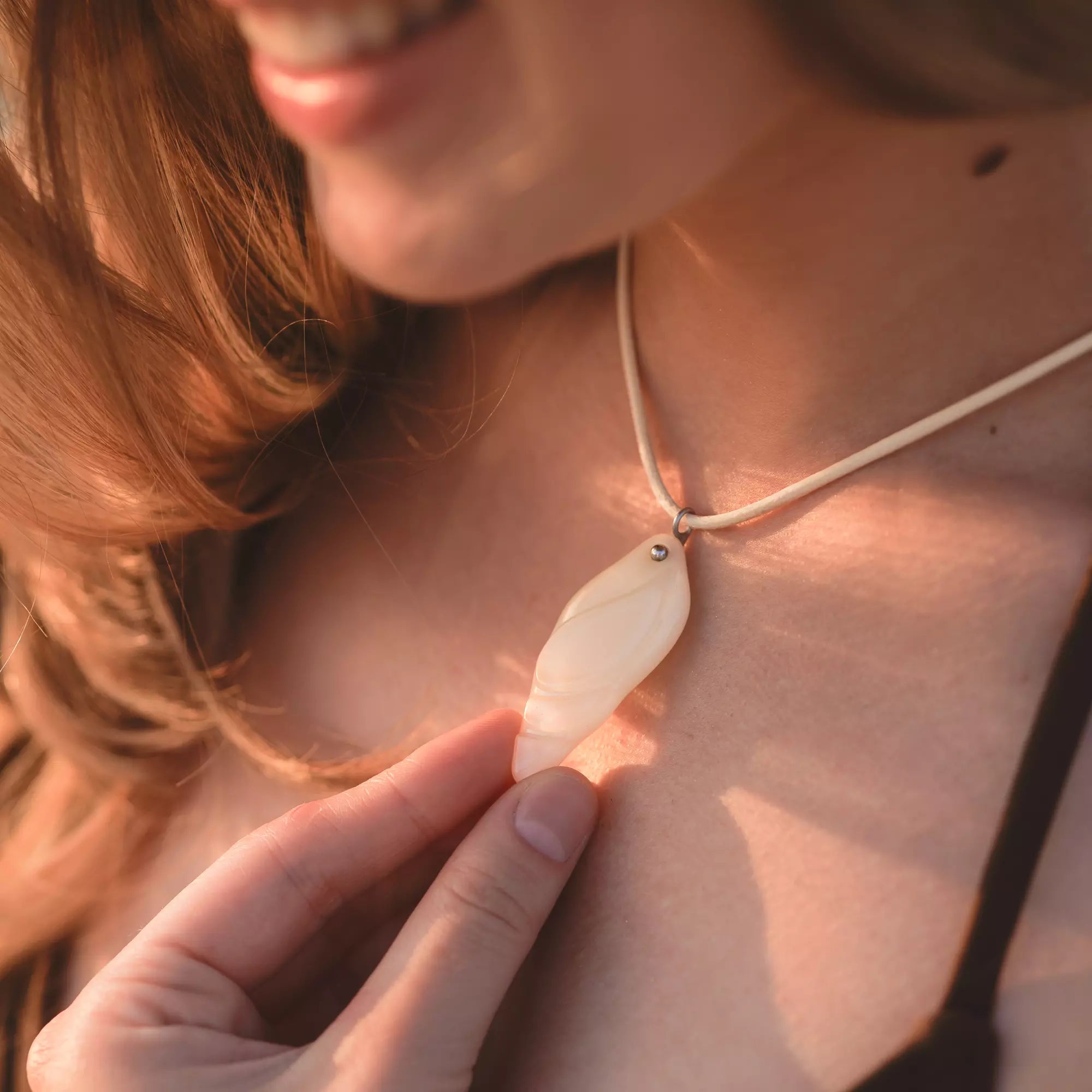 Close-up of a person wearing a necklace with stained glass shell pendant, with a warm glow.