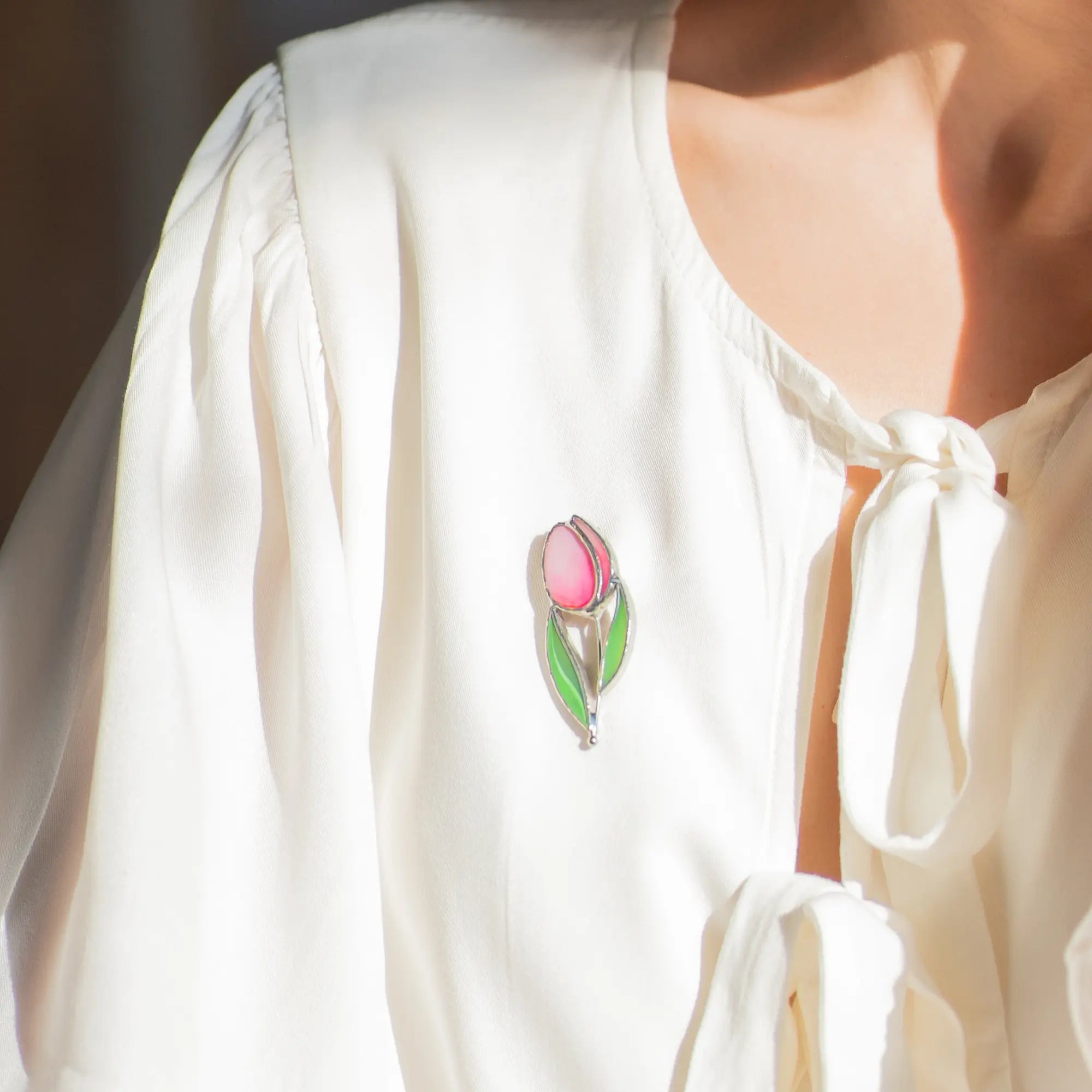 White blouse with a pink tulip flower stained glass brooch on a blurred background