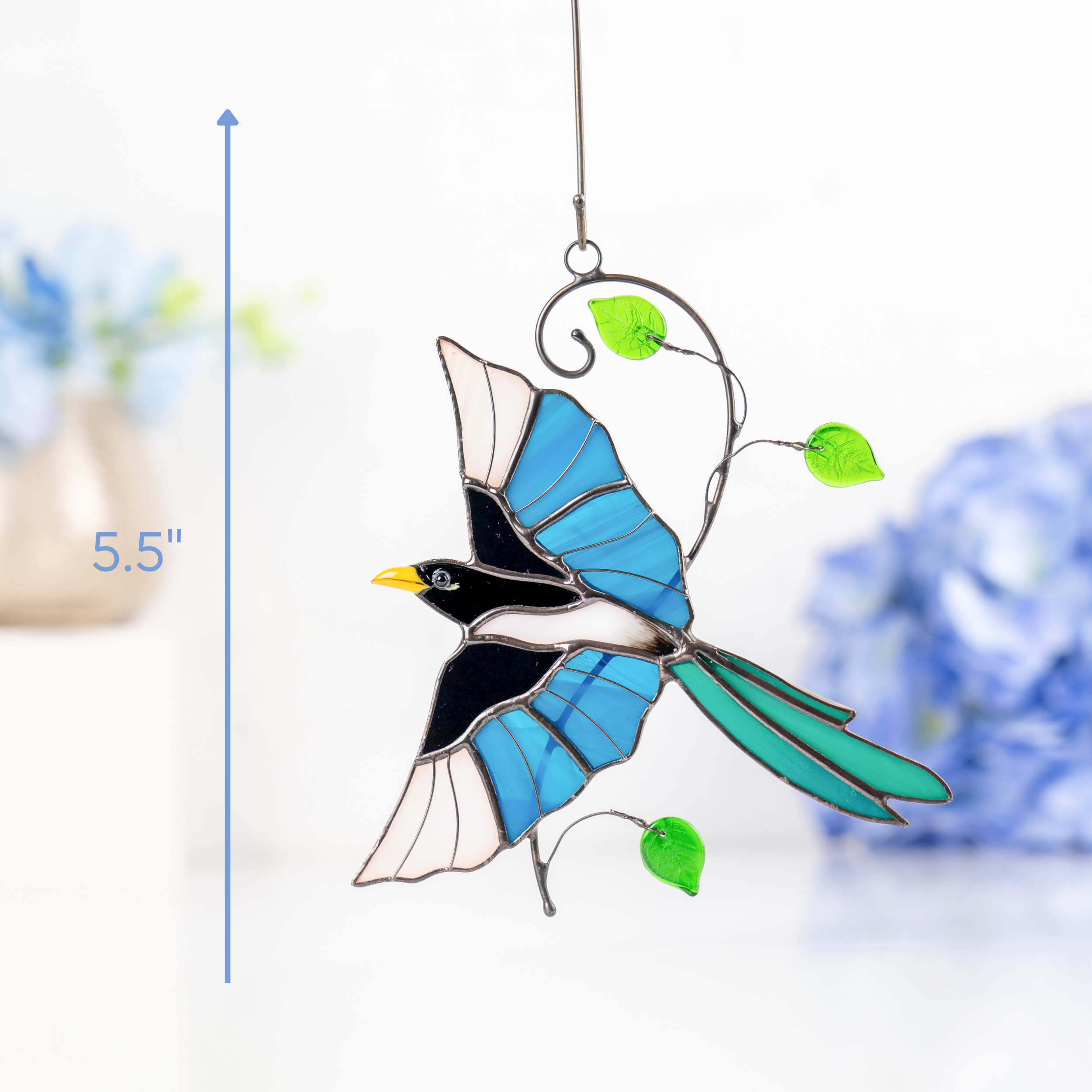 Stained glass magpie suncatcher glowing under light with blue and turquoise details, with height marked as 5.5 inches.