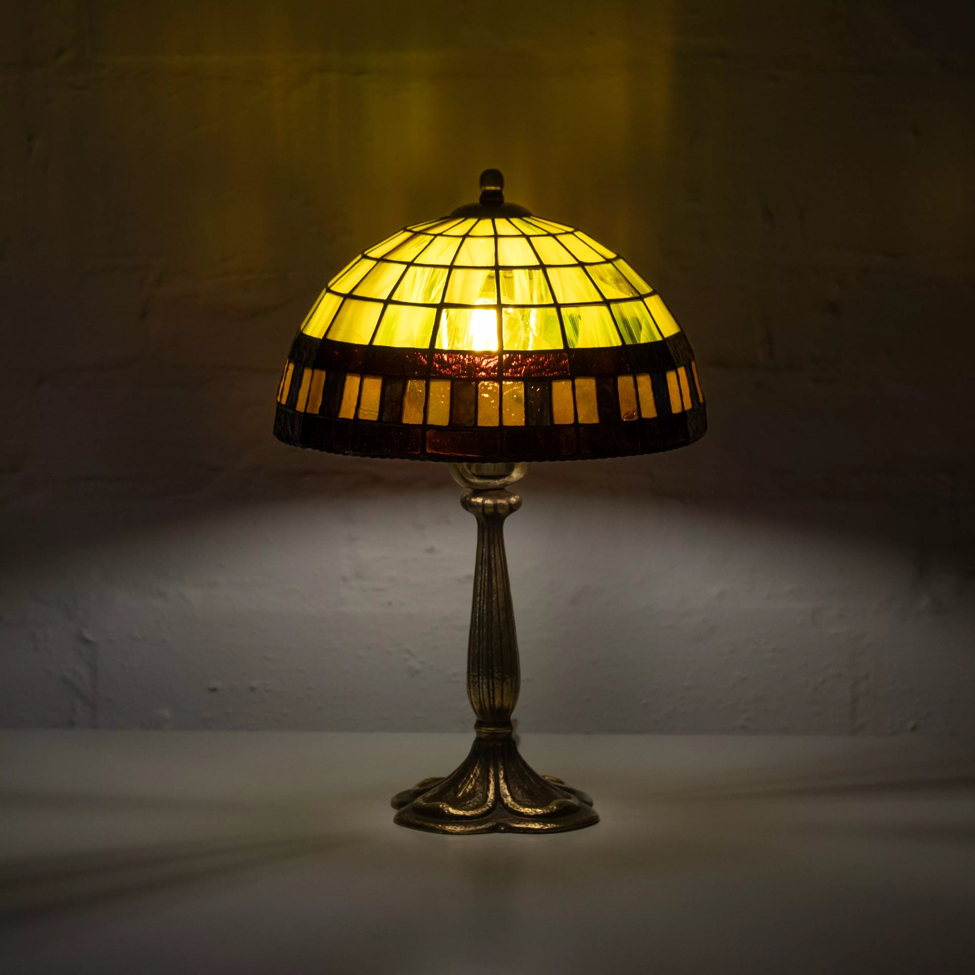 Illuminated yellow stained glass table lamp with amber and black mosaic border on metal base