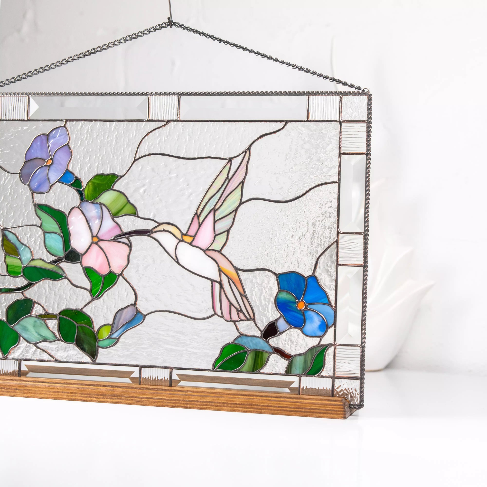Close-up of a pink hummingbird with a blue flower stained glass panel