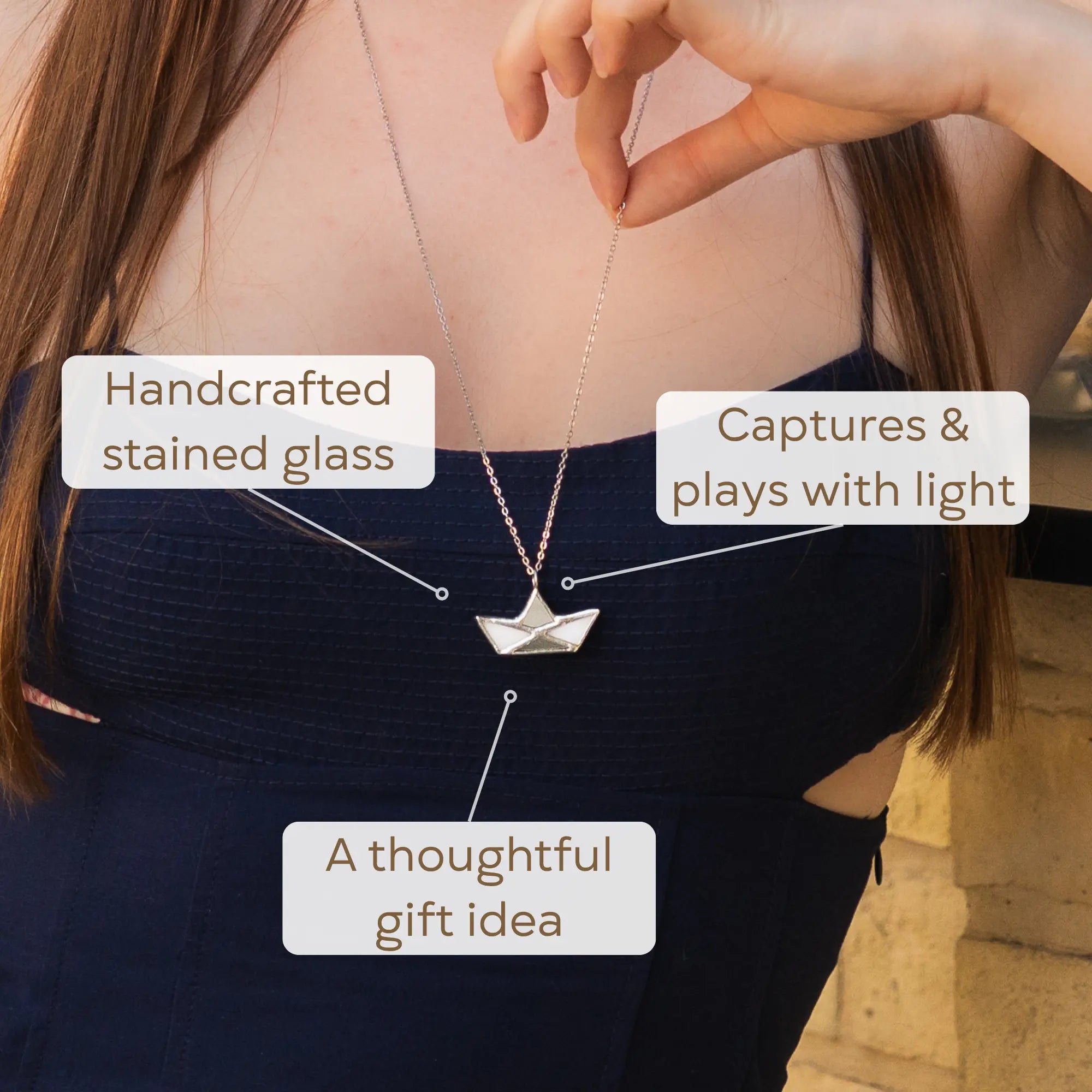 Woman wearing the handmade White Boat stained glass necklace, its luminous white sailboat pendant catching the light against her outfit - Tiffany copper-foil glass jewelry and a thoughtful nautical gift for her