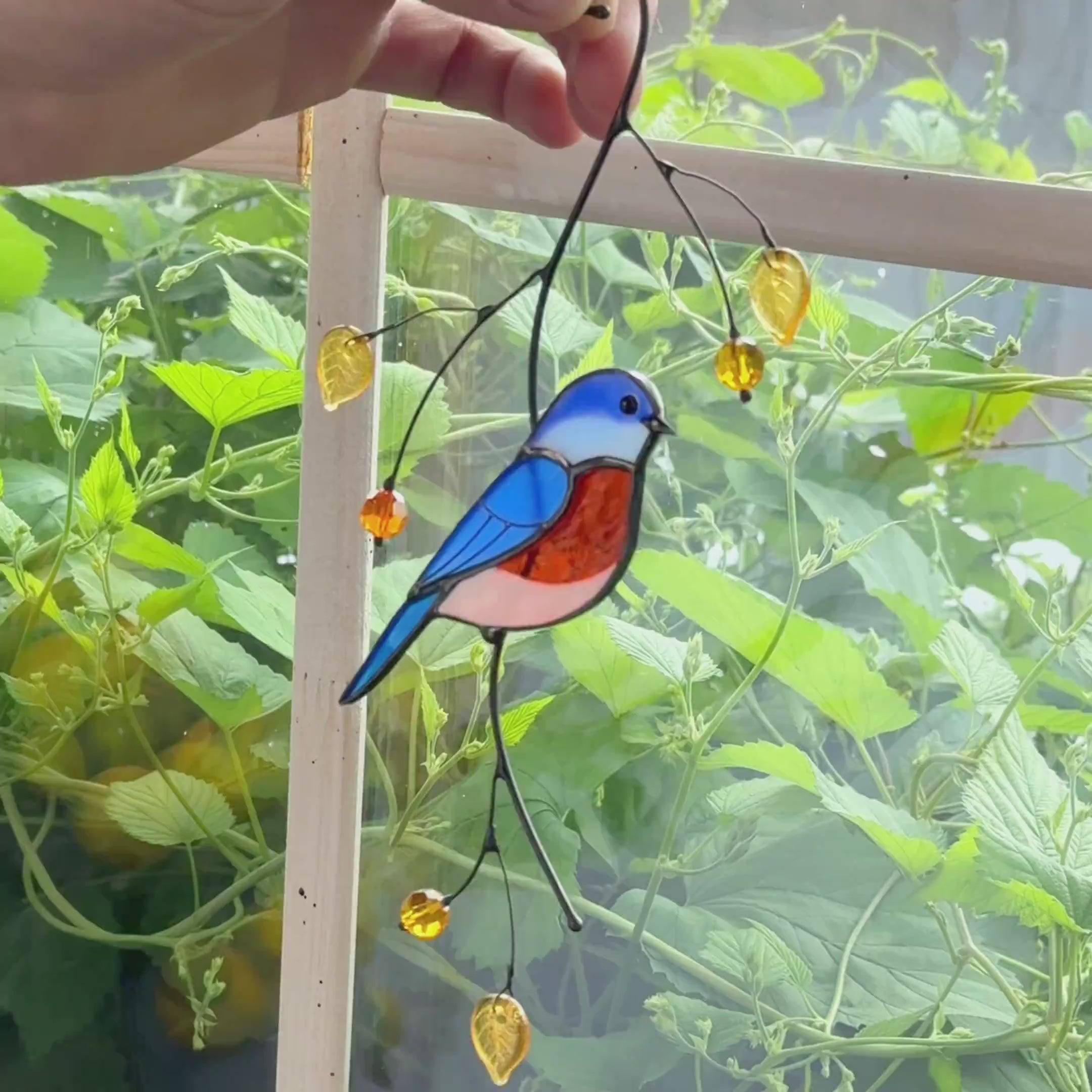 Stained glass bluebird suncatcher perched on a metal branch with golden glass leaves