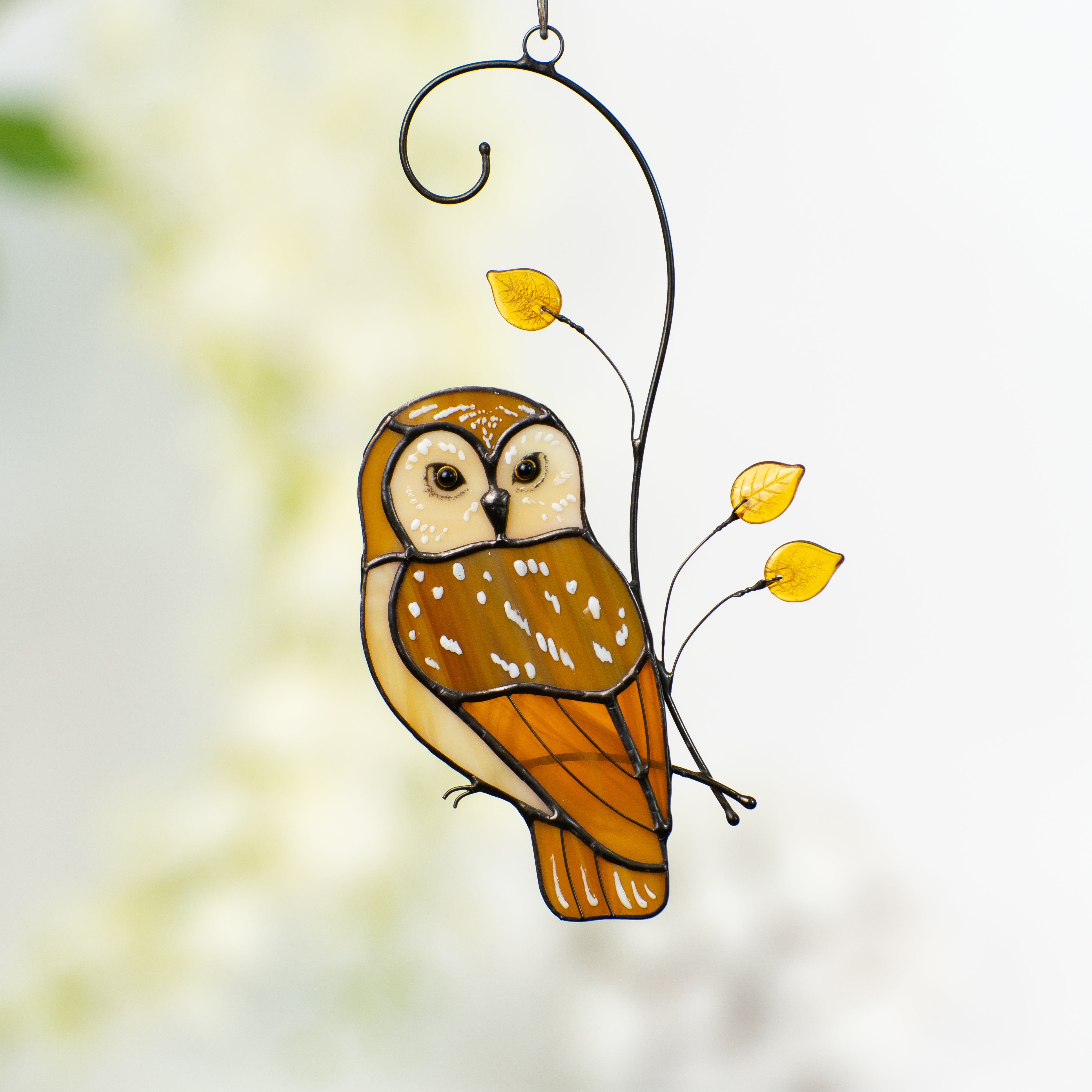 Stained glass owl in warm brown tones with yellow glass leaves, hanging in a softly lit interior