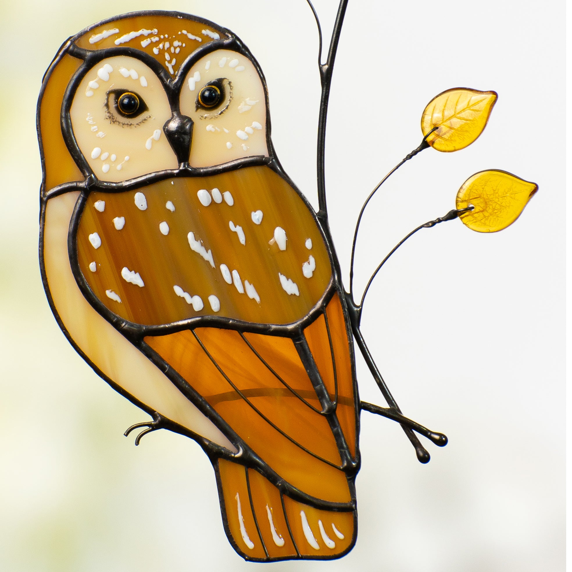 Detailed close-up of owlโs face and body, showing yellow glass leaves and stained glass textures.