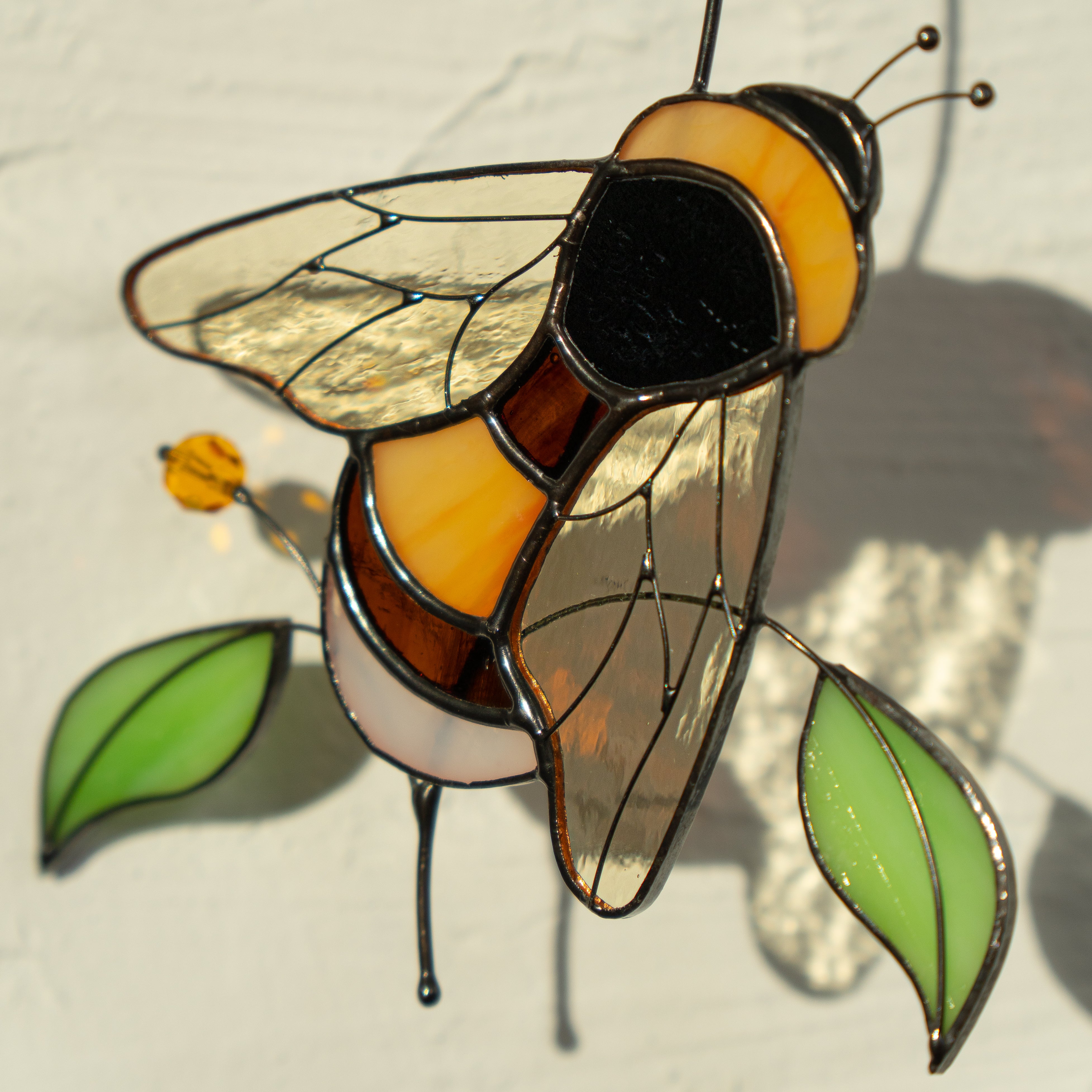 Detailed view of a glass bumble bee suncatcher with golden wings and green leaves.