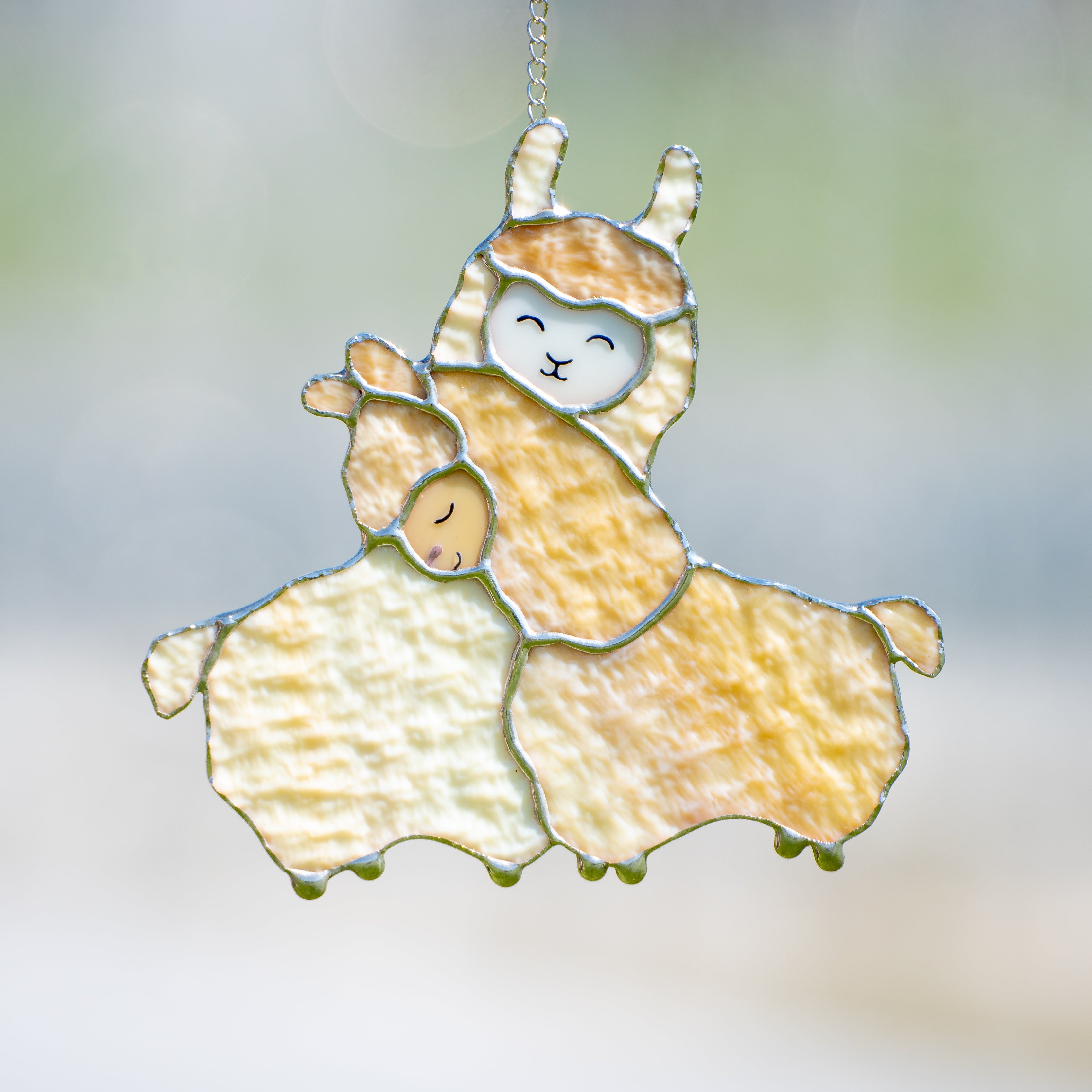 Stained glass window hanging of two beige llamas cuddling