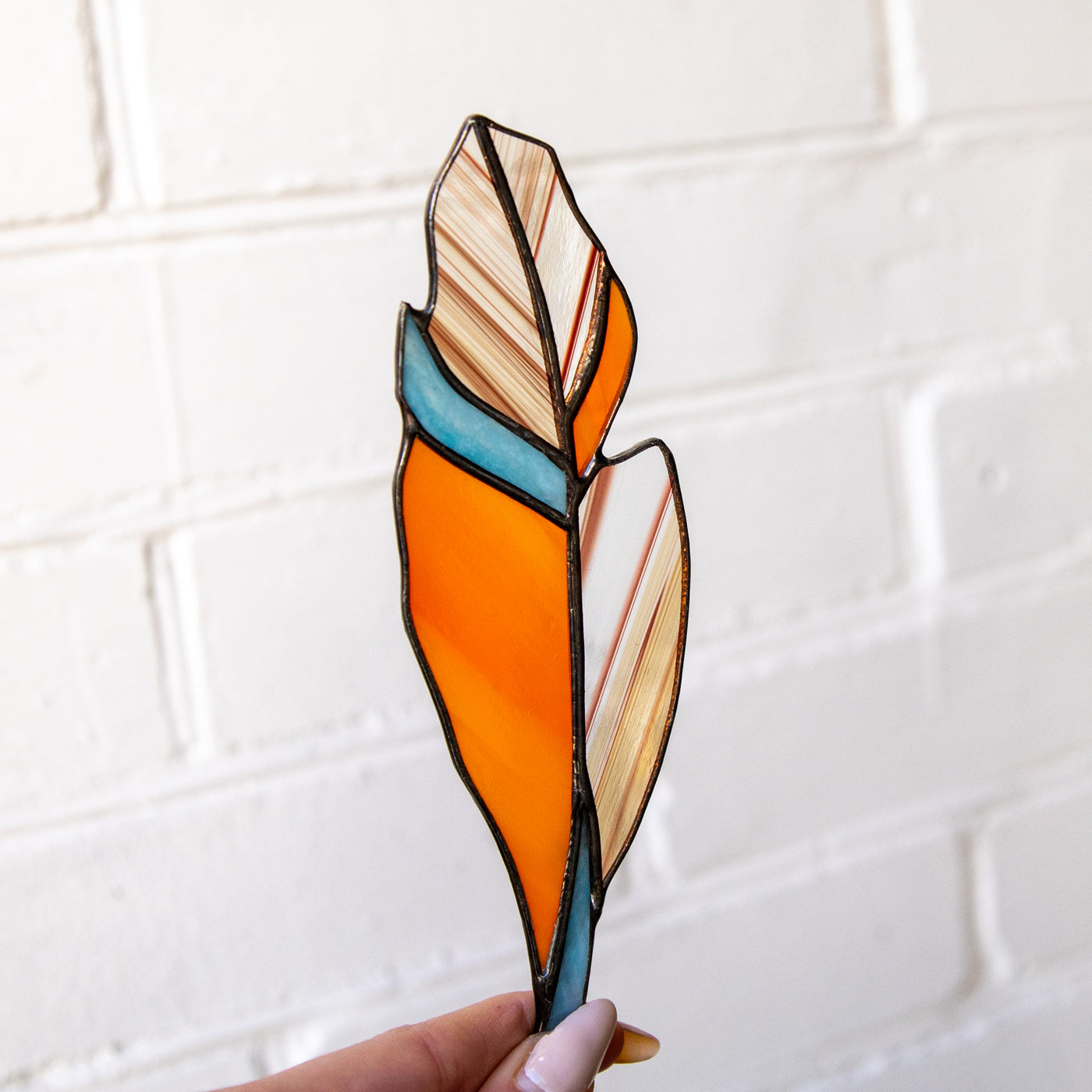 Stained glass orange feather suncatcher with blue parts and blotchiness