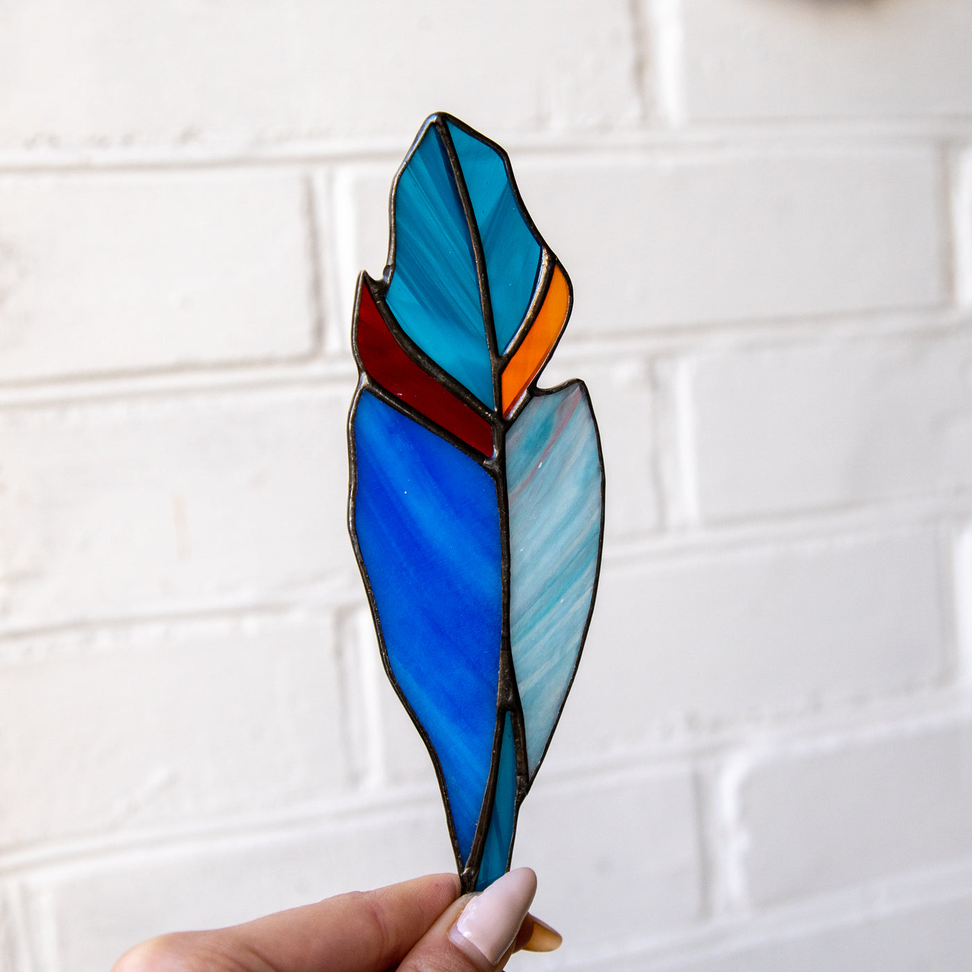 Stained glass feather of blue shades and red and orange parts suncatcher