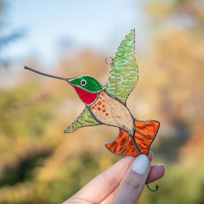 Bright hummingbird suncatcher of stained glass with green wings and orange tail