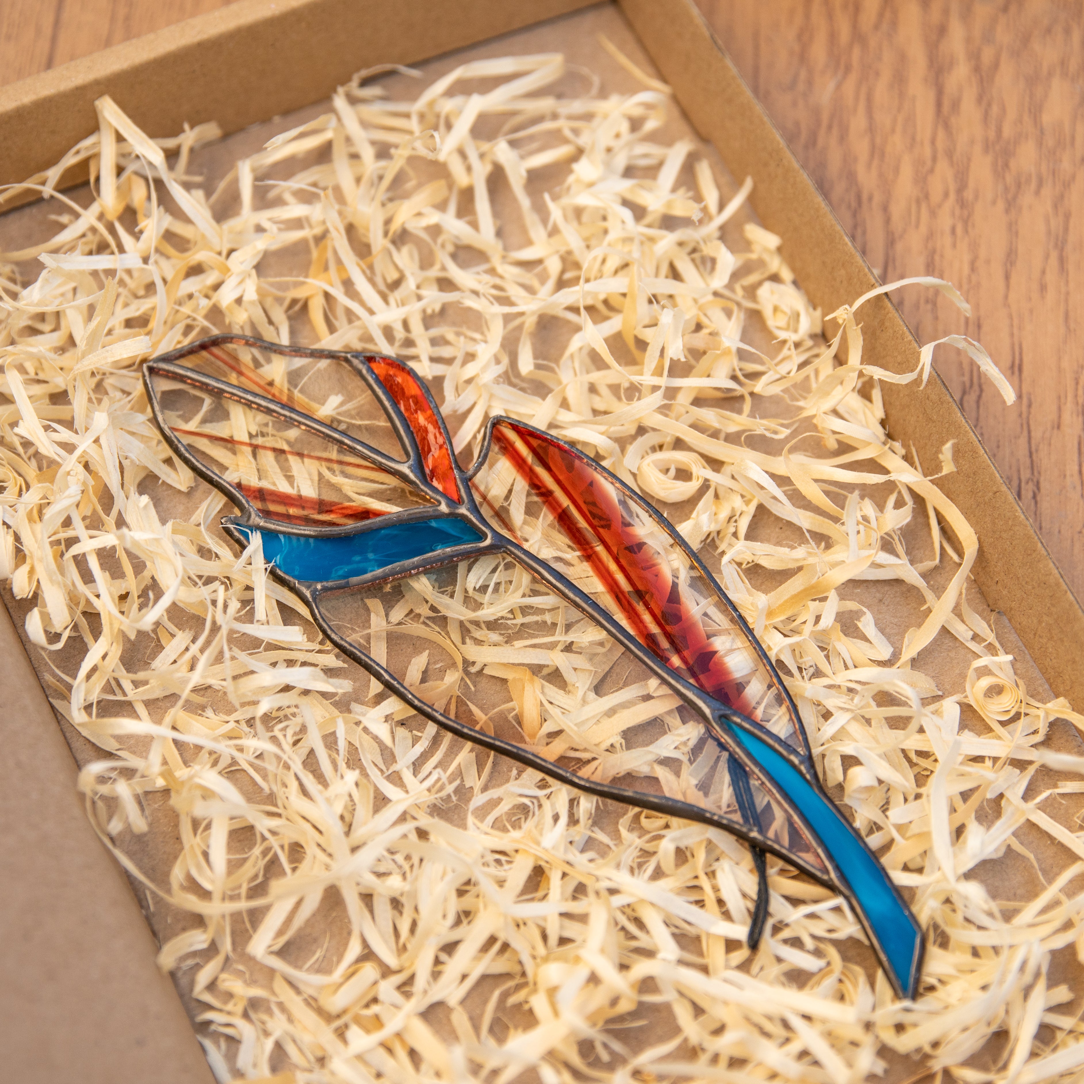 Clear stained glass feather window hanging with blue and orange parts and blotchiness