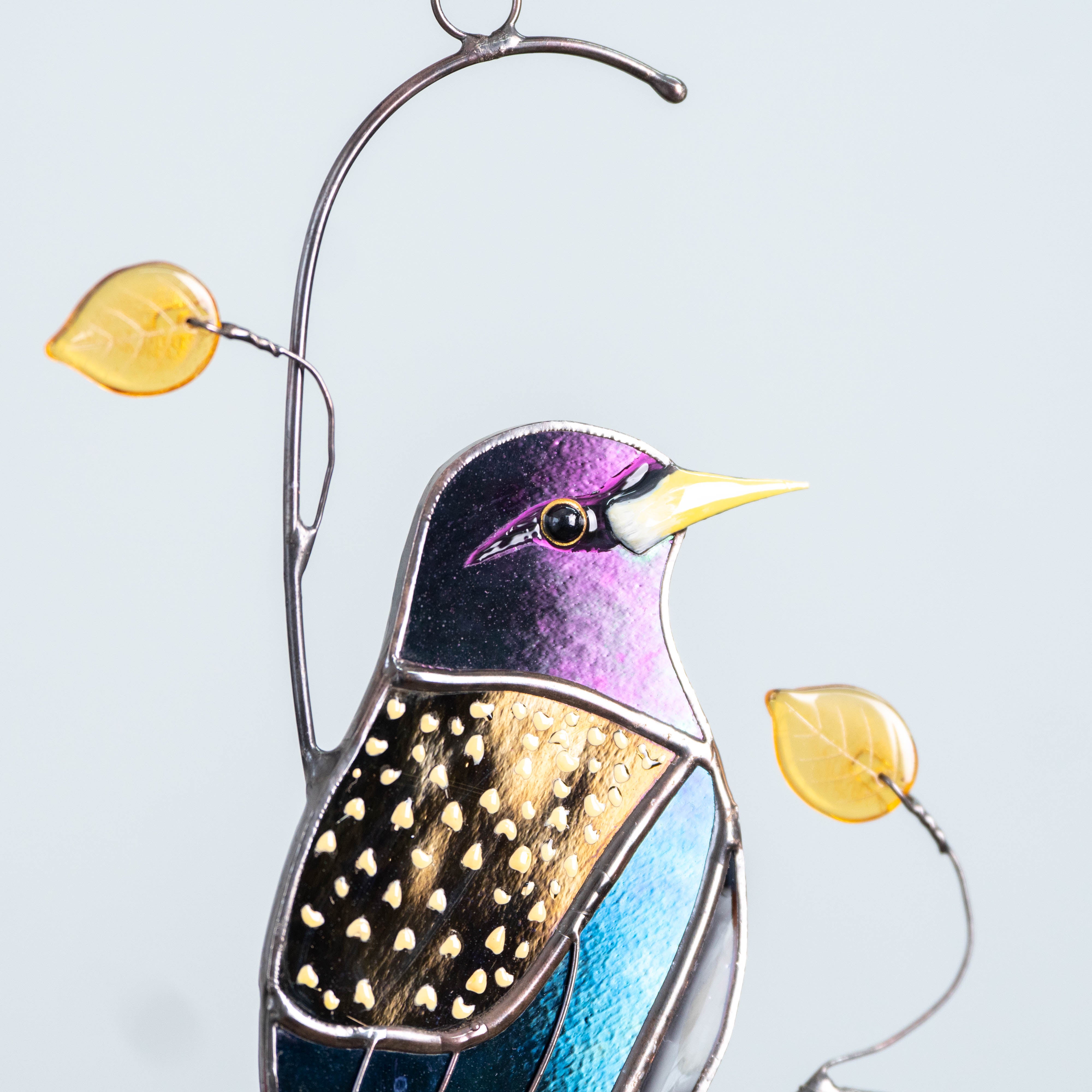 Side view of robin glass suncatcher with warm-colored leaves, hanging with white background.