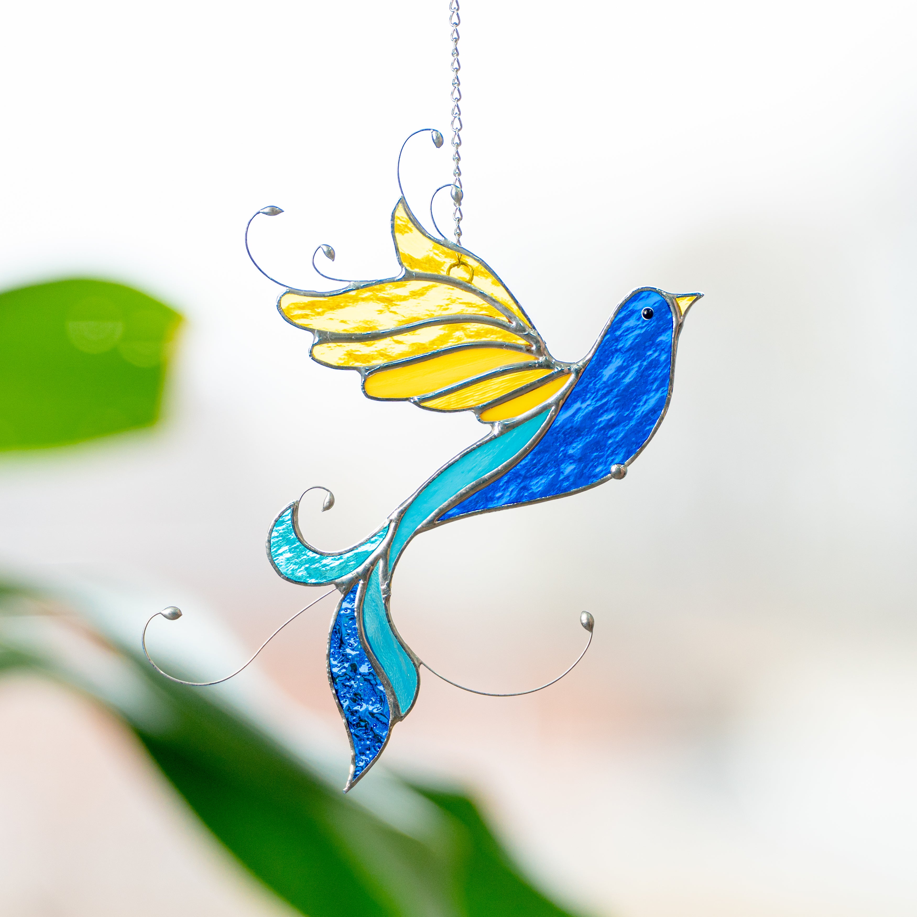 Ukrainian bird window hanging Stained glass suncatcher bird in Ukrainian colors hanging near a green plant in daylight.