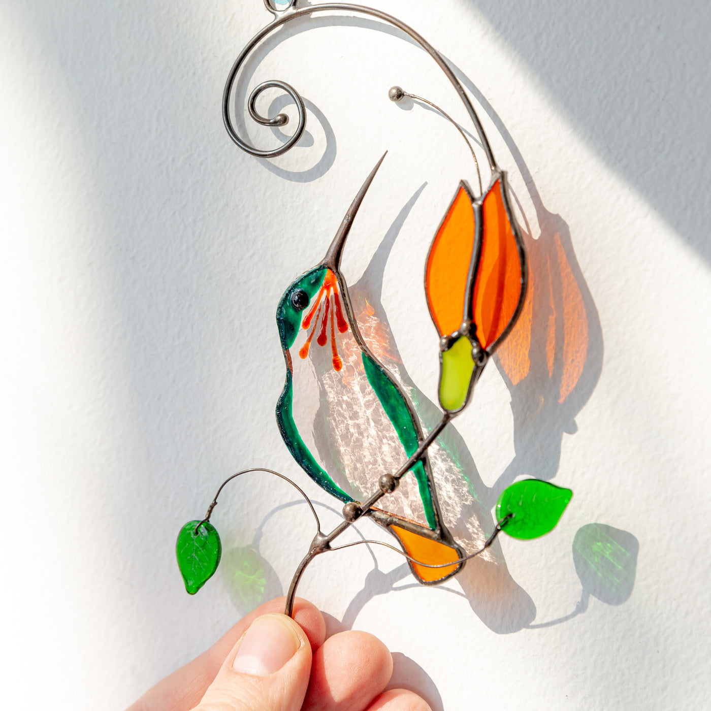 Window hanging of a stained glass hummingbird on the branch with orange flower