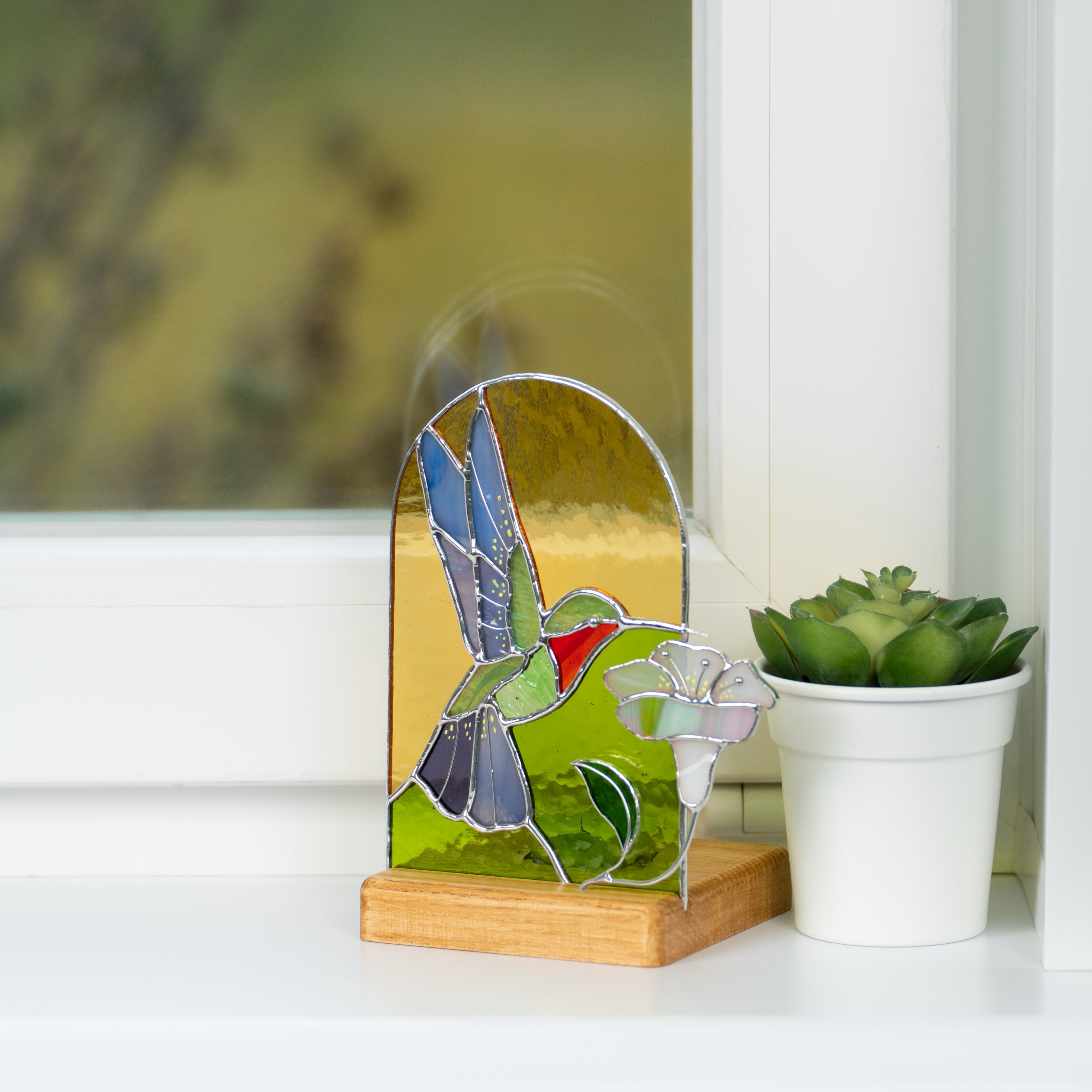 Stained glass candle-lit panel of a flying hummingbird on a window