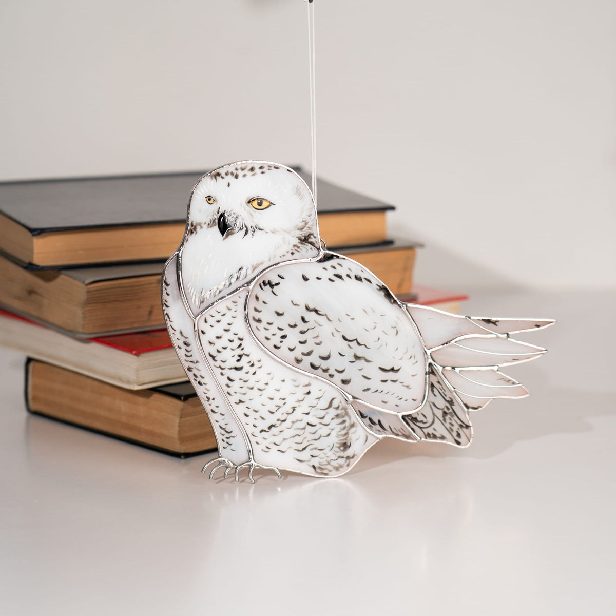 White stained glass owl suncatcher hanging beside a stack of books