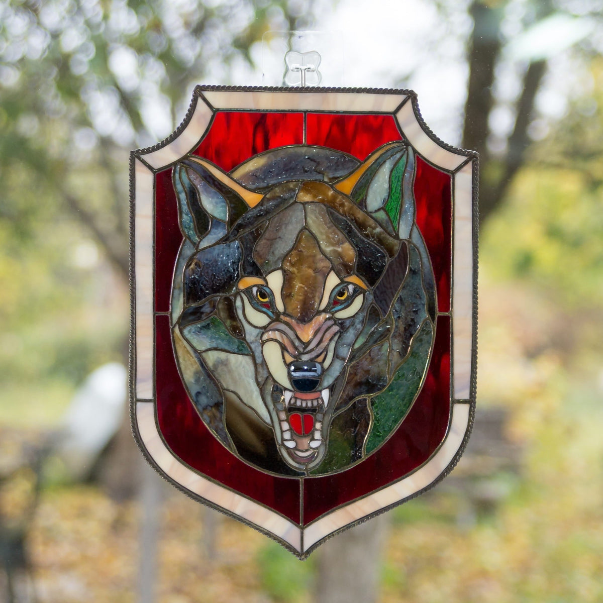 Stained glass wolf head suncatcher on a red shield, symbol of strength