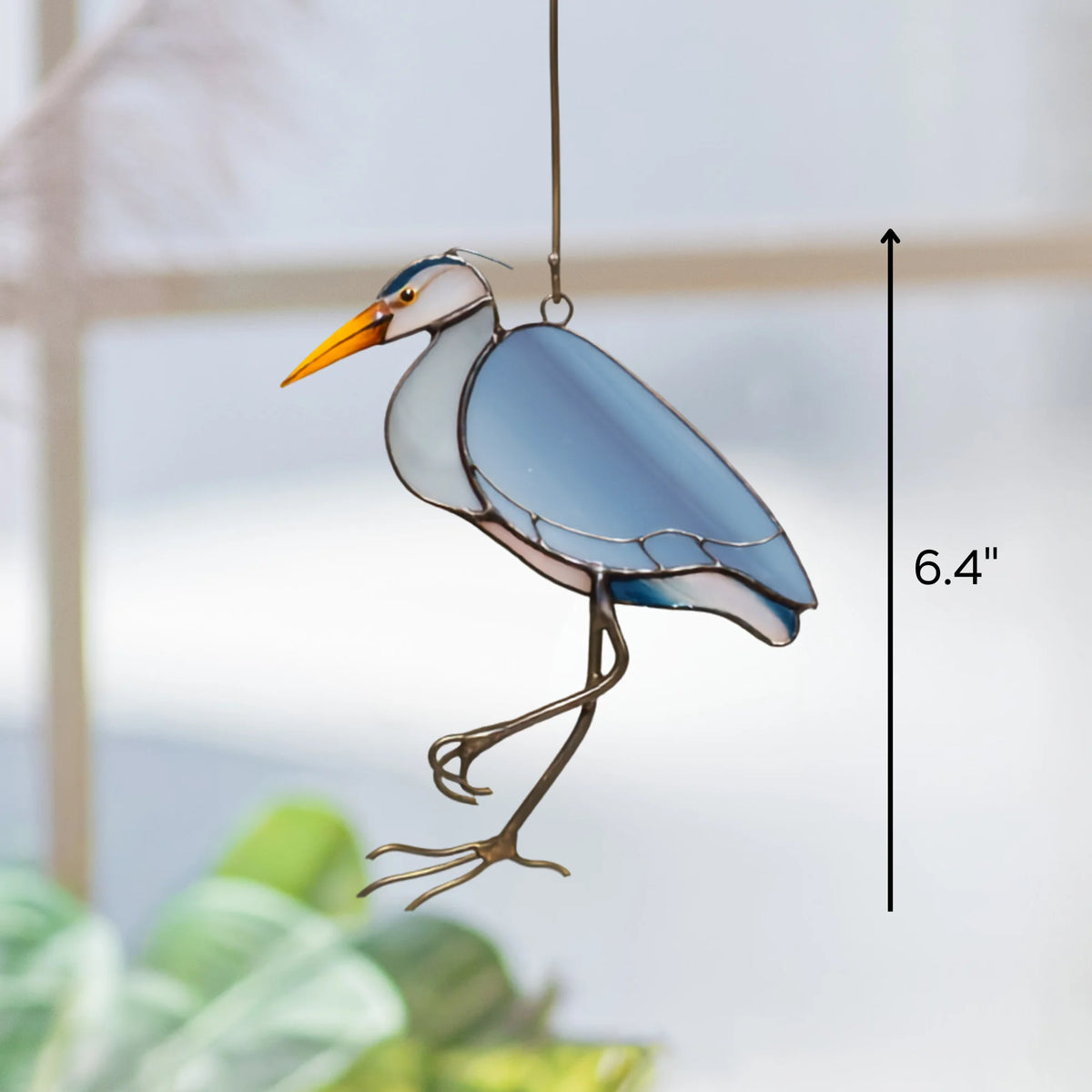 Great Blue Heron suncatcher hanging by a window, 6.4 inches tall - handmade stained glass bird with blue wings, a white neck and a bright orange beak catching the daylight