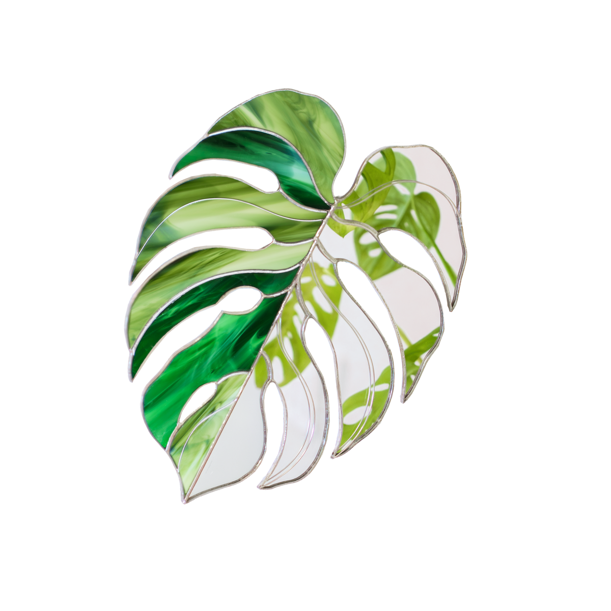 Monstera Leaf Stained Glass Mirror on a white background - one half swirled emerald and lime green glass, the other half mirror reflecting a leafy plant, a handmade stained glass wall mirror