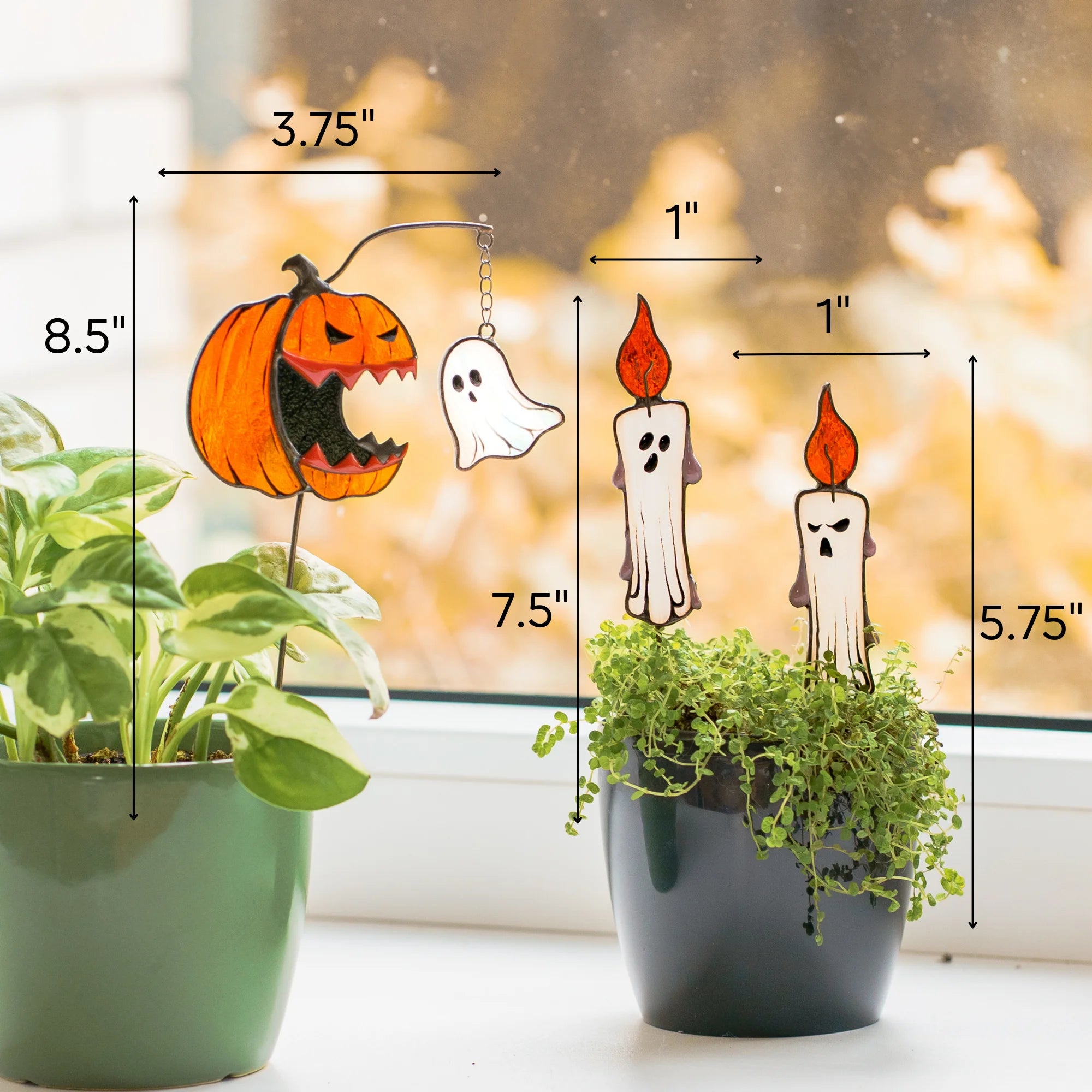 Halloween-themed stained glass ornaments displayed on potted plants in front of a window, with dimension callouts showing the pumpkin-and-ghost ornament as 8.5 by 3.75, and candles sized 1 by 7.5 and 1 by 5.75 inches
