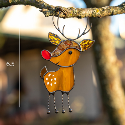 Handmade stained glass reindeer hanging from a branch outdoors with size marker indicating 6.5 inches tall.