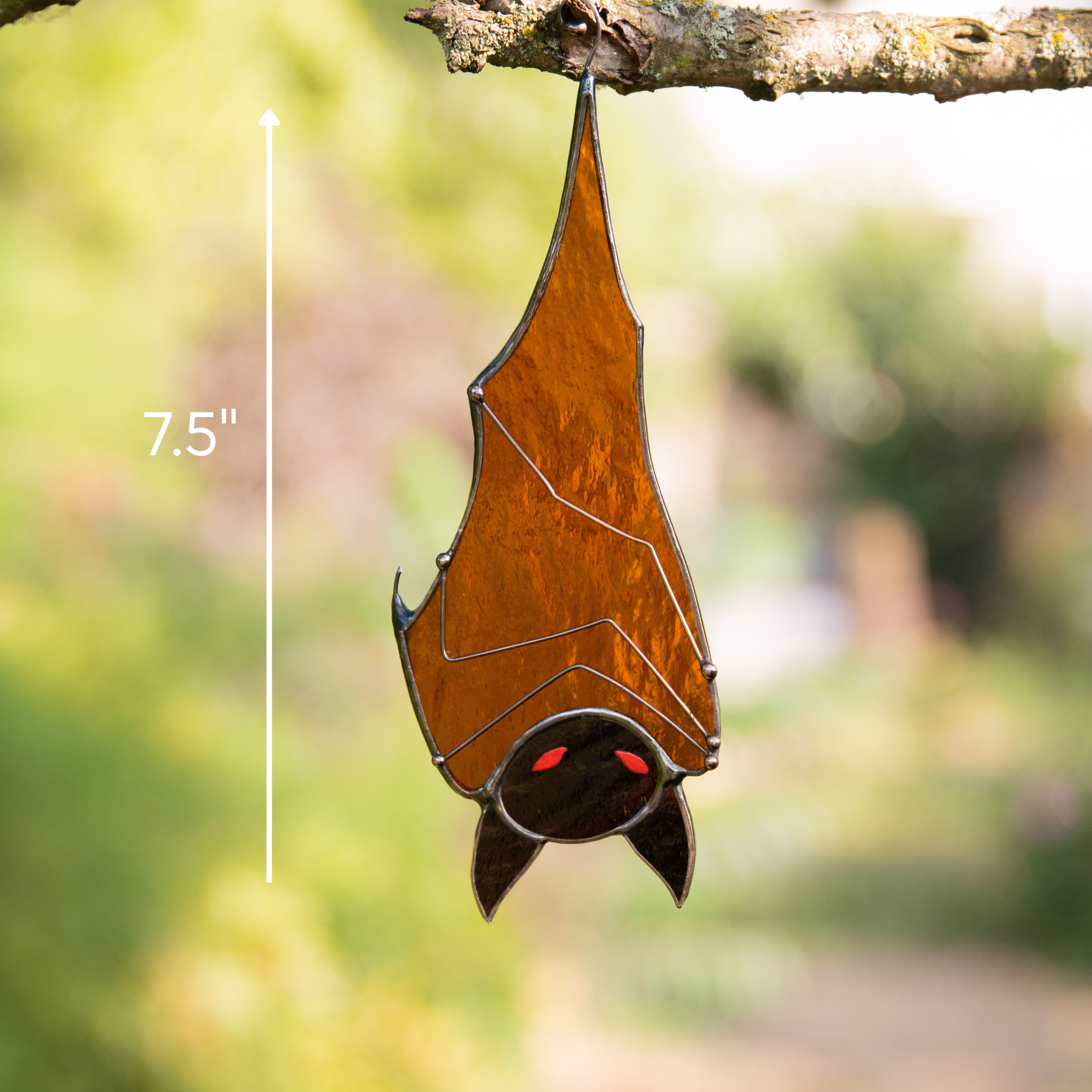 Glass bat hanging from tree branch outdoors with size marker showing 7.5" height.