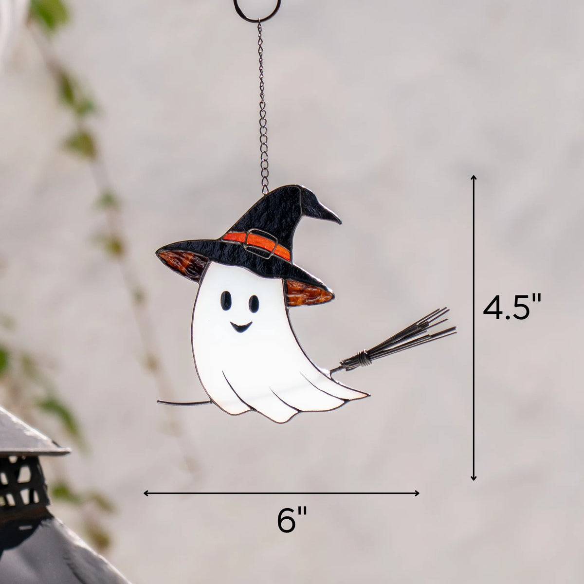Size chart for the Halloween stained glass ghost suncatcher - 6 inches wide by 4.5 inches tall including chain and ring, shown against a blurred garden background