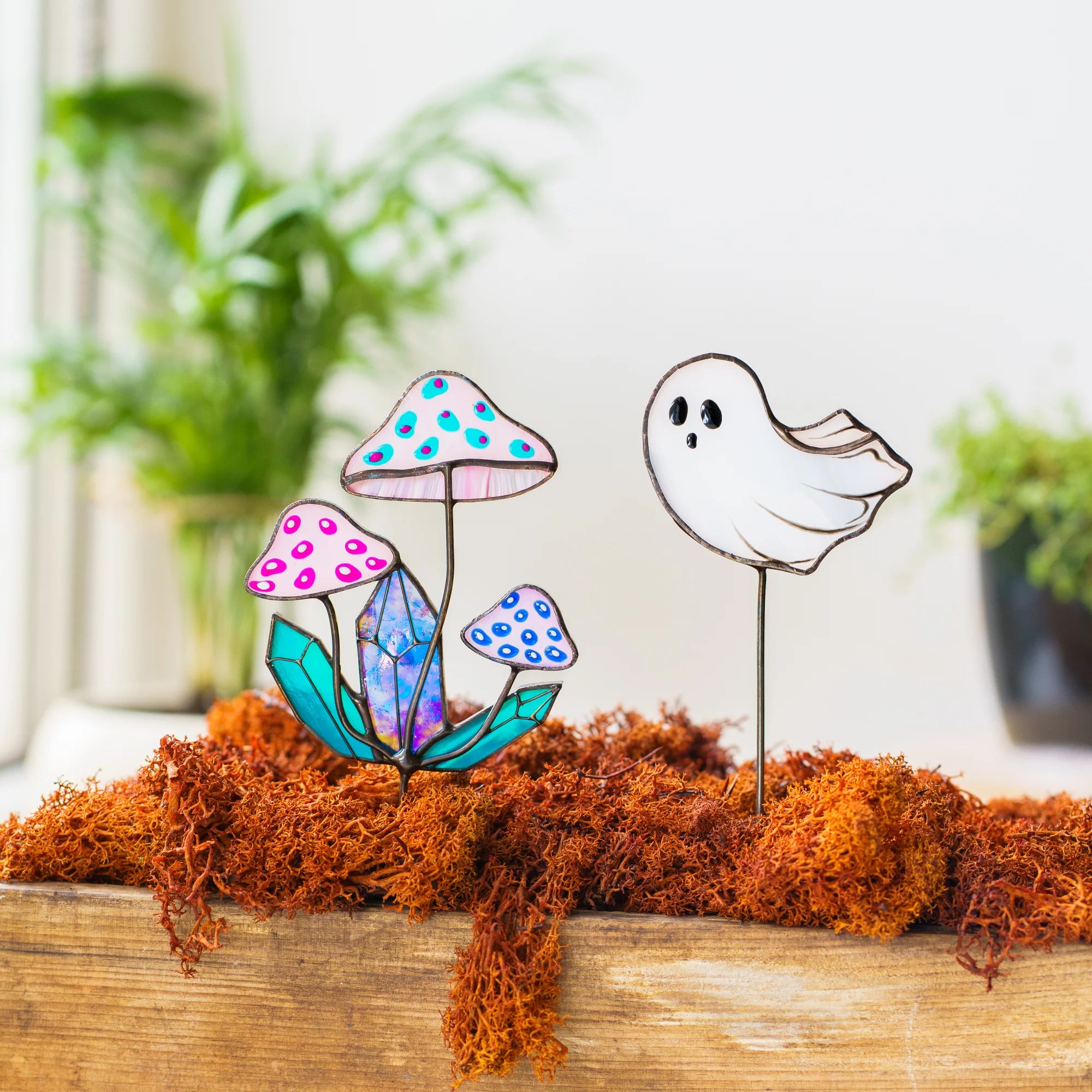 Handmade stained glass plant stakes in a mossy wooden box - a cluster of pink opal toadstools with turquoise and blue spots growing around a crystal, next to a floating white ghost