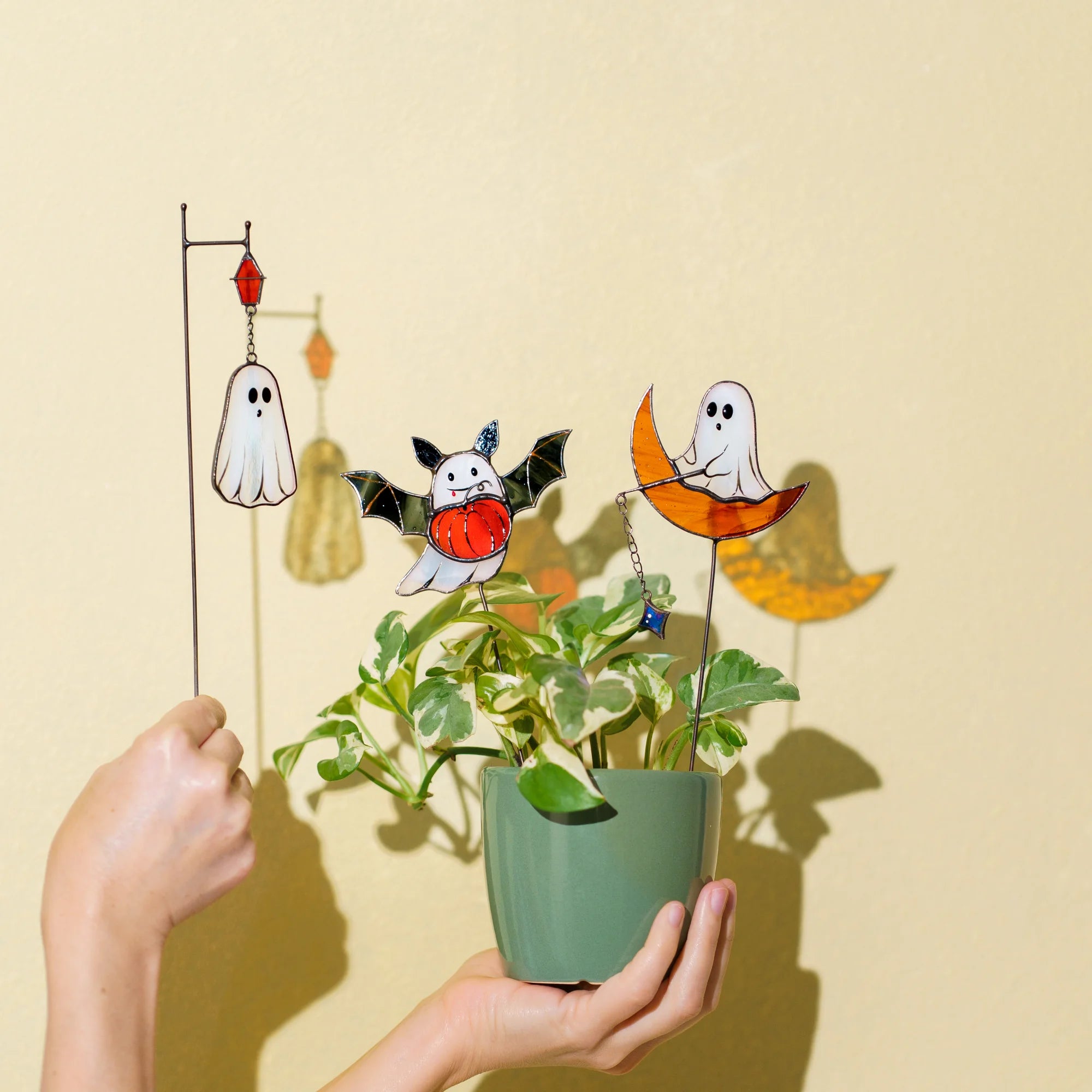 A person holding handcrafted stained glass Halloween plant stakes featuring friendly ghosts, making it a thoughtful and spooky gift option.