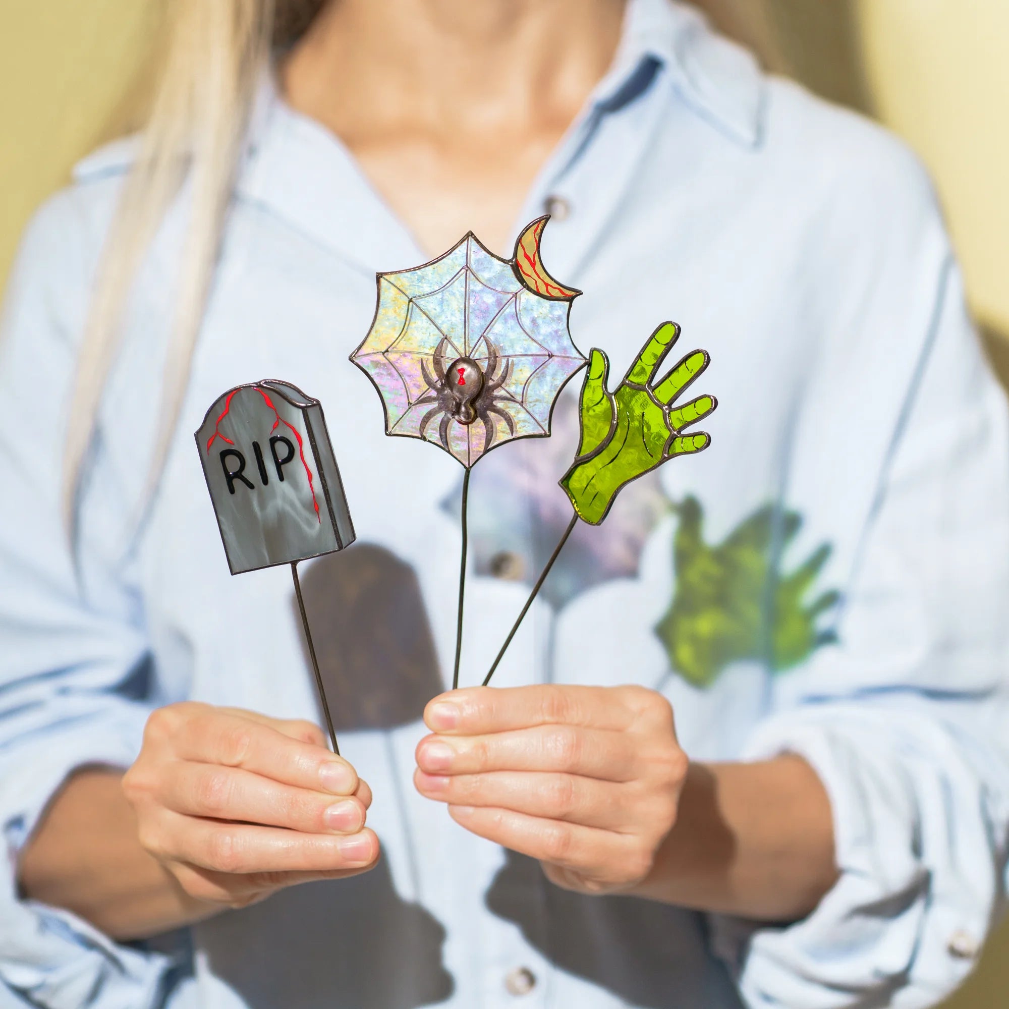A person holding handmade stained glass Halloween plant stakes, showcasing them as a thoughtful and spooky gift option.