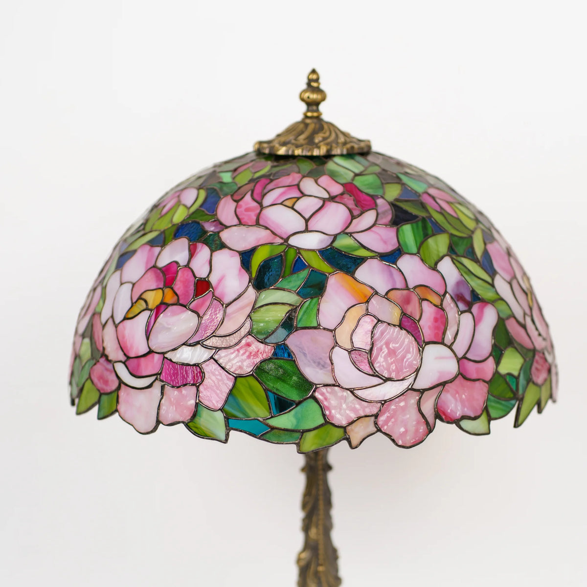 Stained glass peony table lamp shade on a white background, angled view showing pink, white and green glass petals with a scalloped edge and brass finial - handmade Tiffany style lighting