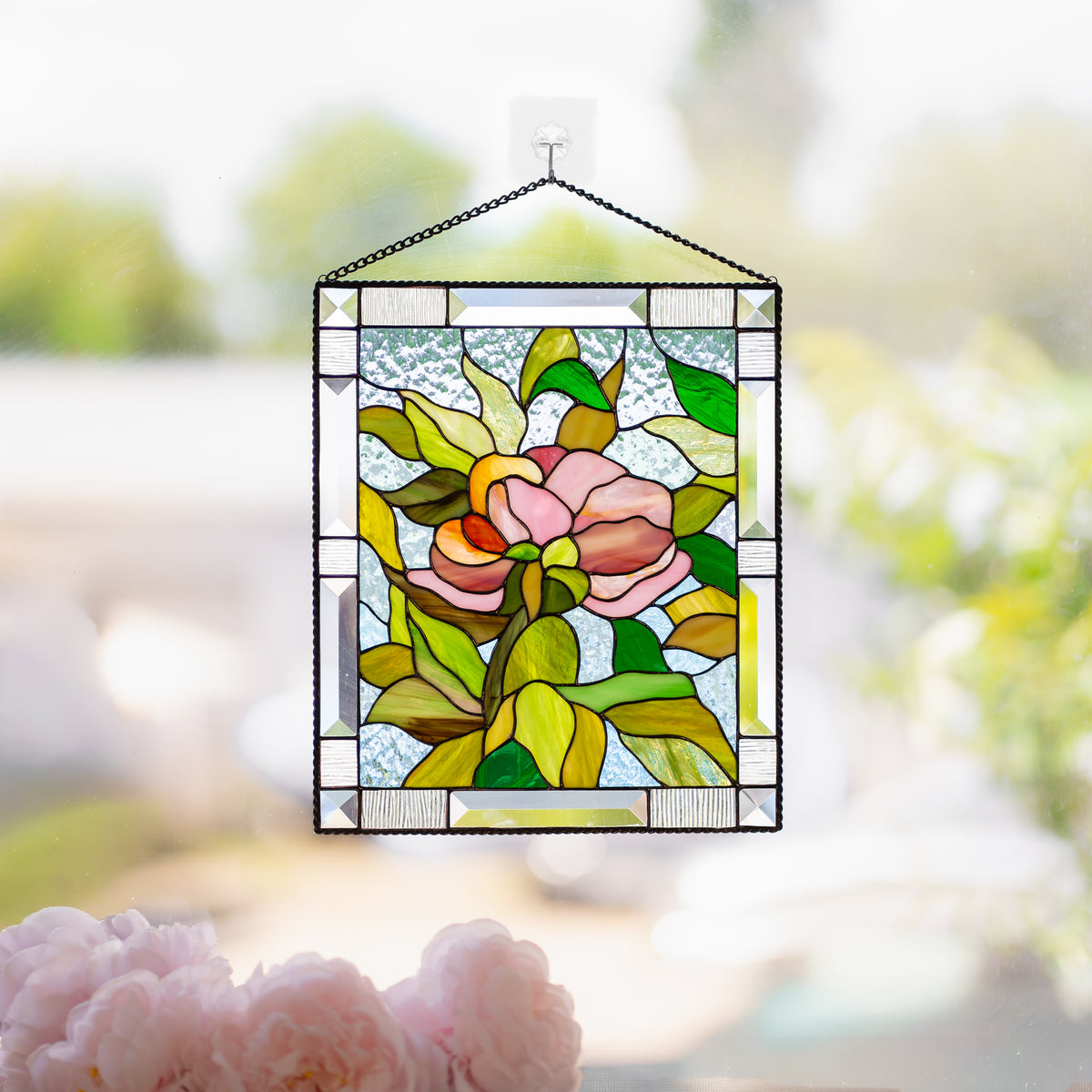 Woman hanging a stained glass peony panel with beveled clear glass border on a window using a suction cup hook.