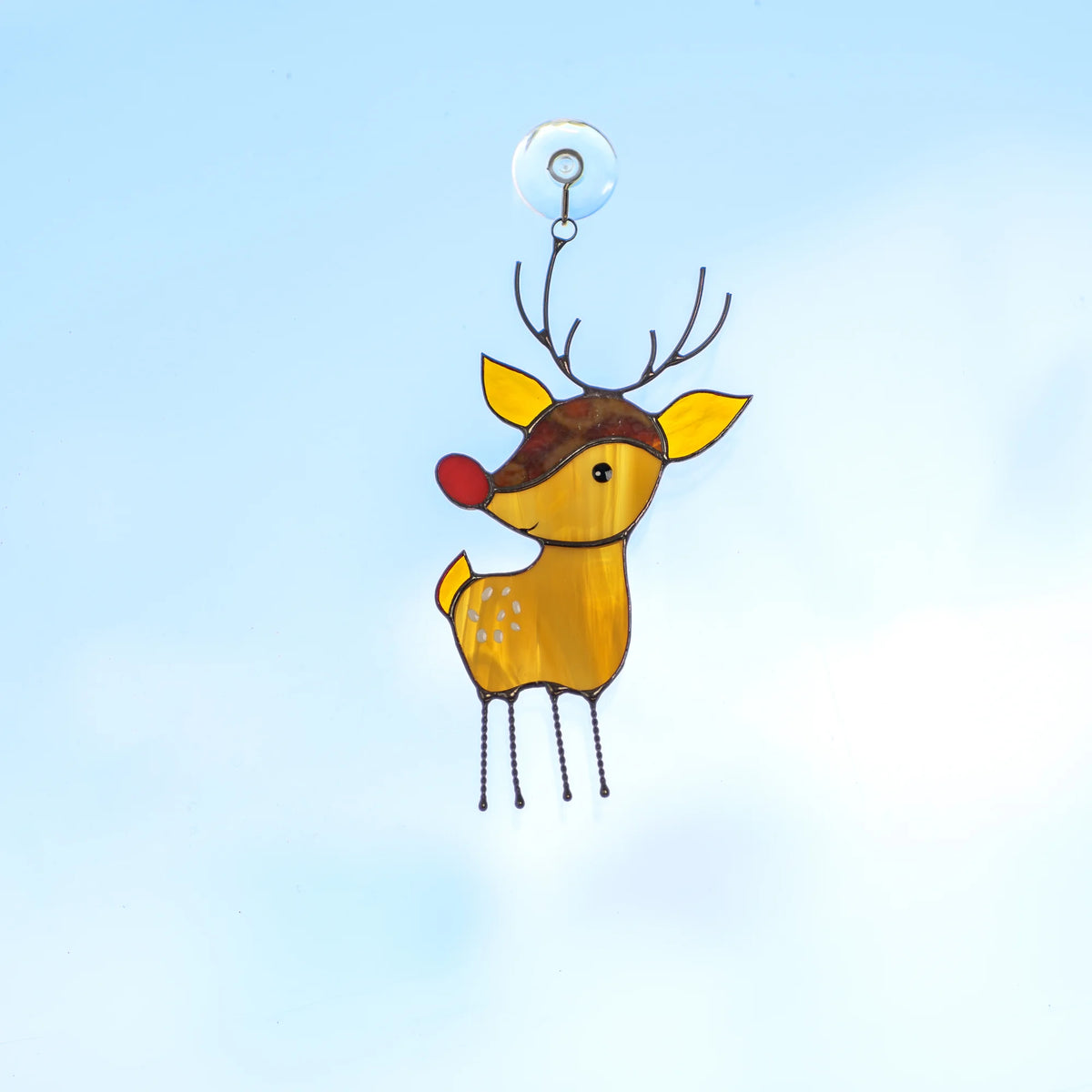 Stained glass reindeer suncatcher with a red nose and branching antlers hanging from a suction cup against a clear blue sky.