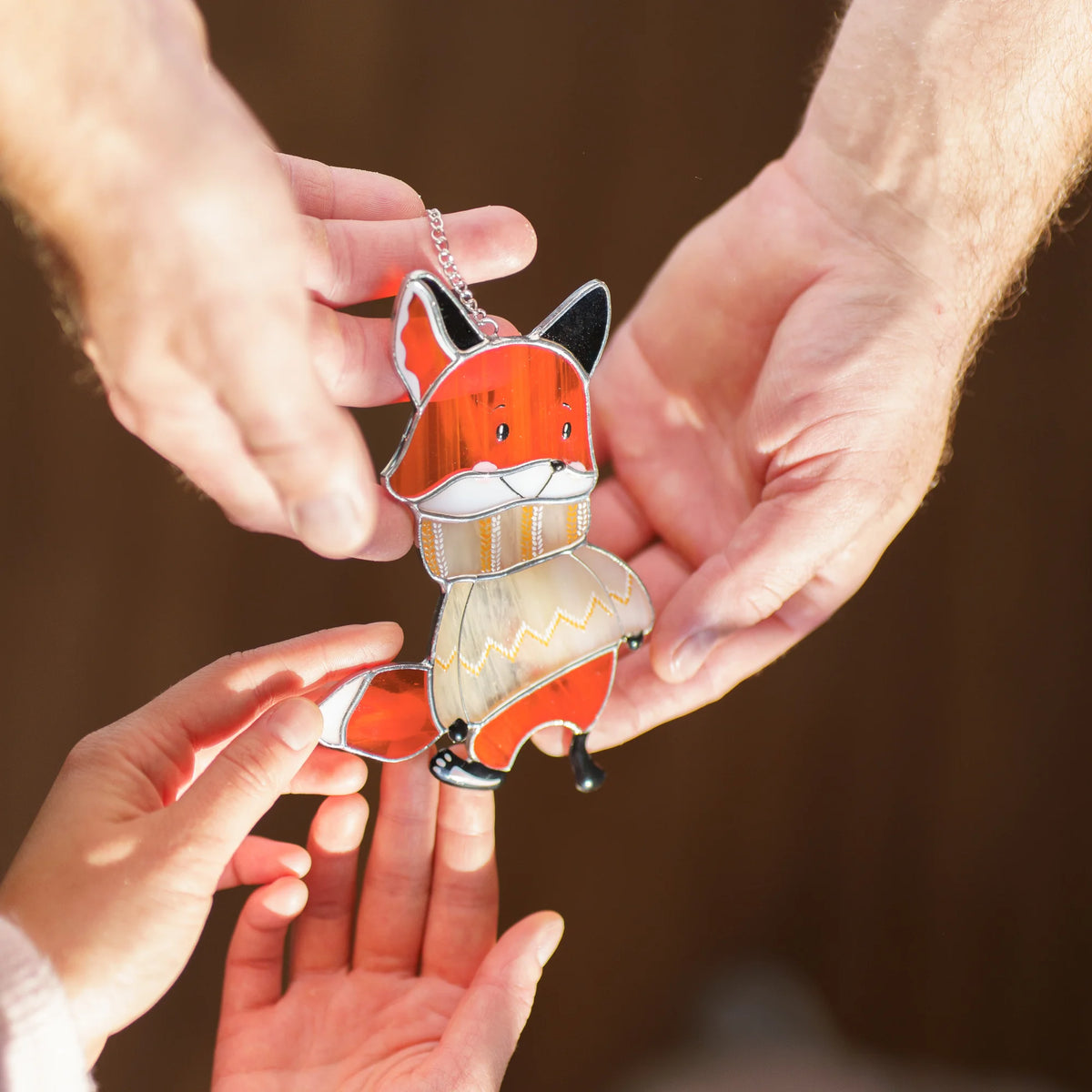 Man holding up a stained glass fox suncatcher in a sweater to show a woman, both smiling during a playful Christmas moment.