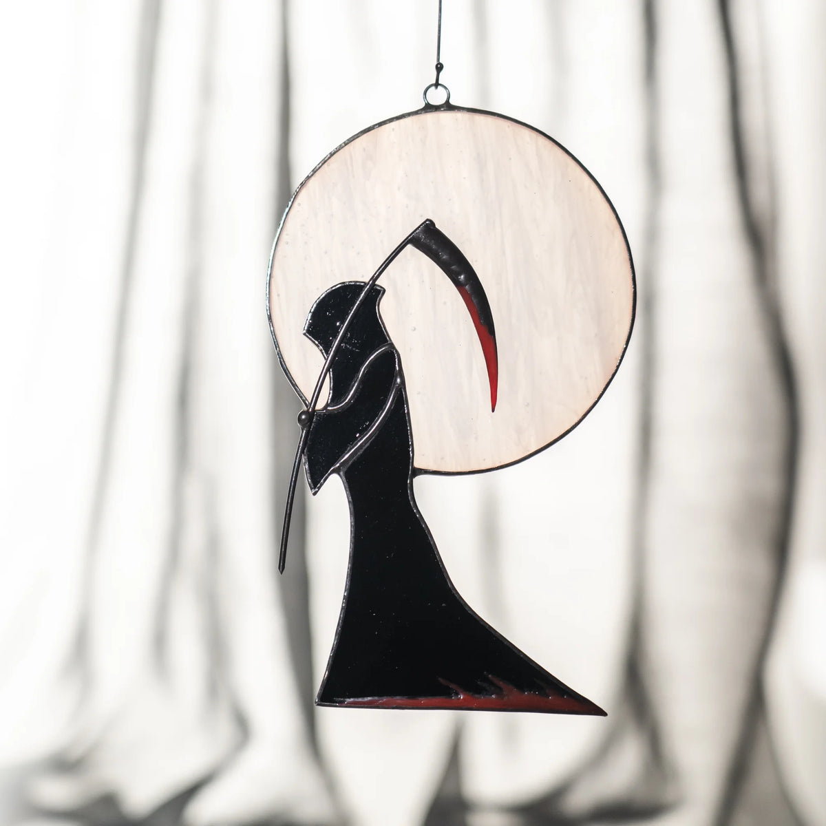 Handmade Grim Reaper and moon stained glass window hanging suspended in front of a soft white curtain - gothic Halloween window decor for a bedroom or hallway
