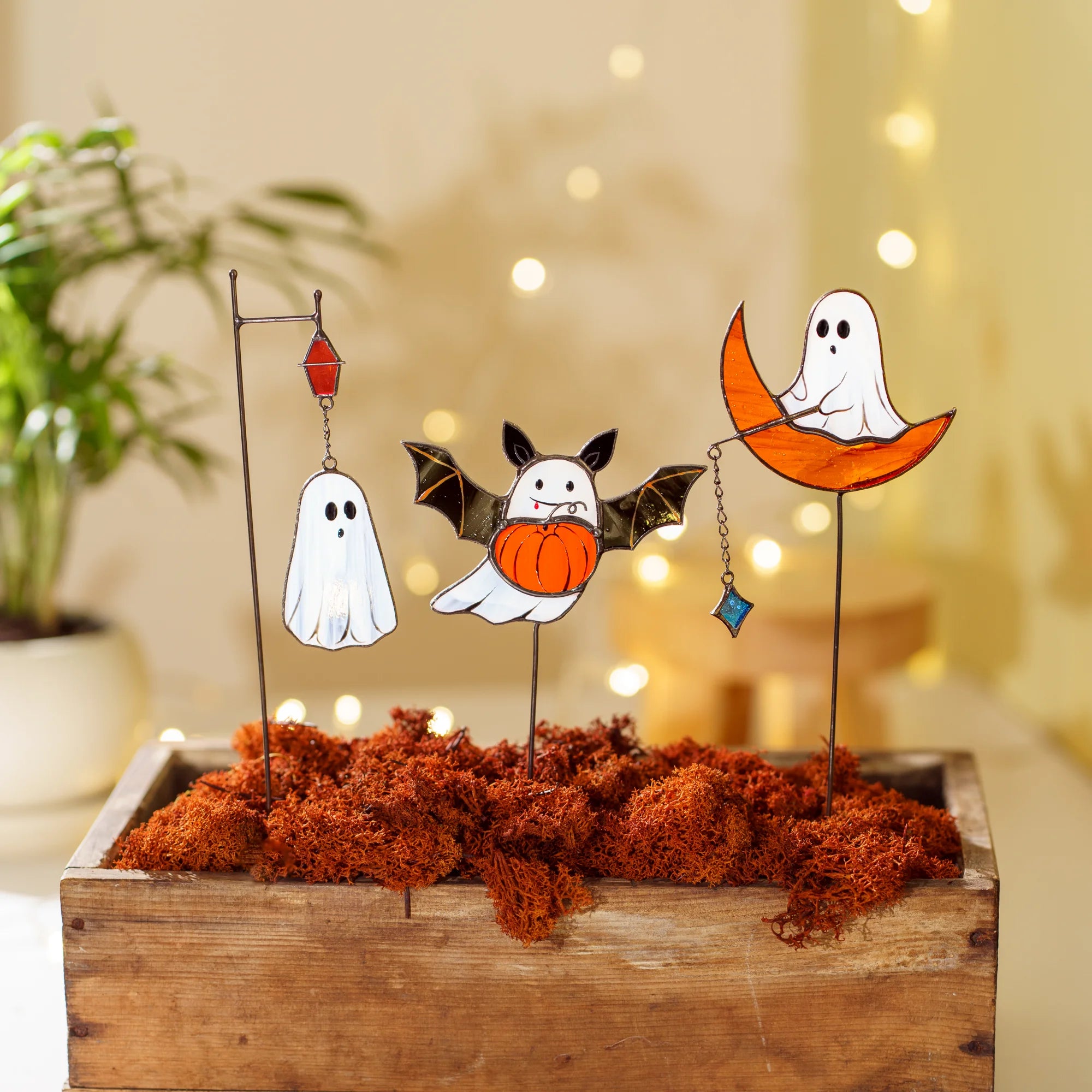 A wooden box filled with decorative orange moss and Halloween stained glass plant stakes with ghosts, serving as a charming gift choice.
