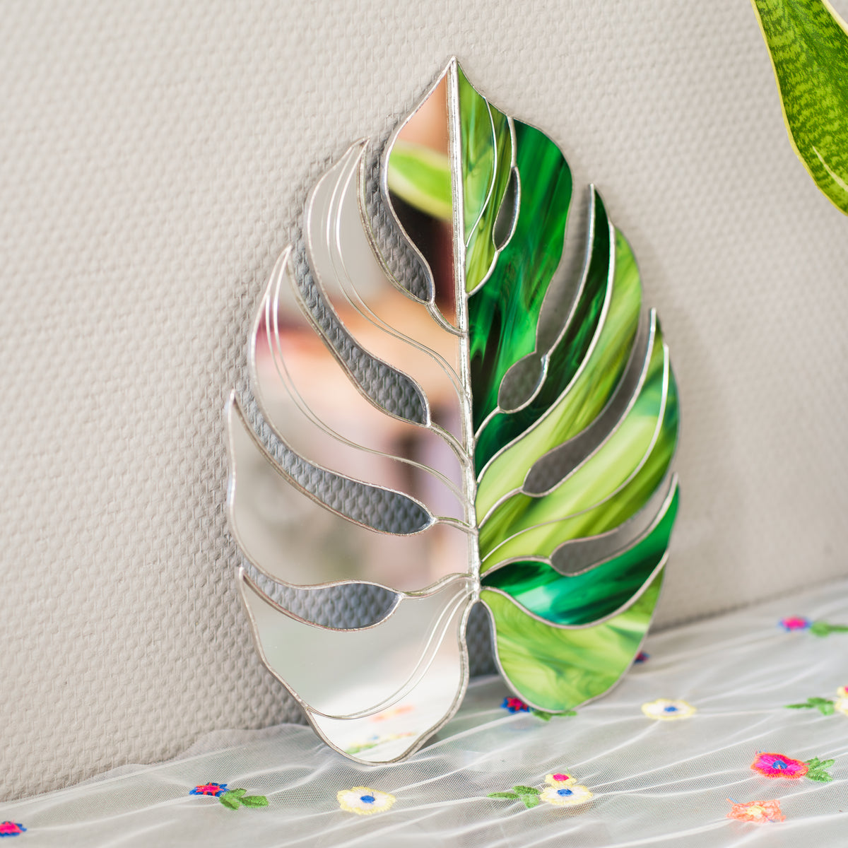 Close-up of the Monstera Leaf Stained Glass Mirror standing upright, showing swirled green glass, mirror segments and silver soldered veins - handmade mirror stained glass and botanical wall art