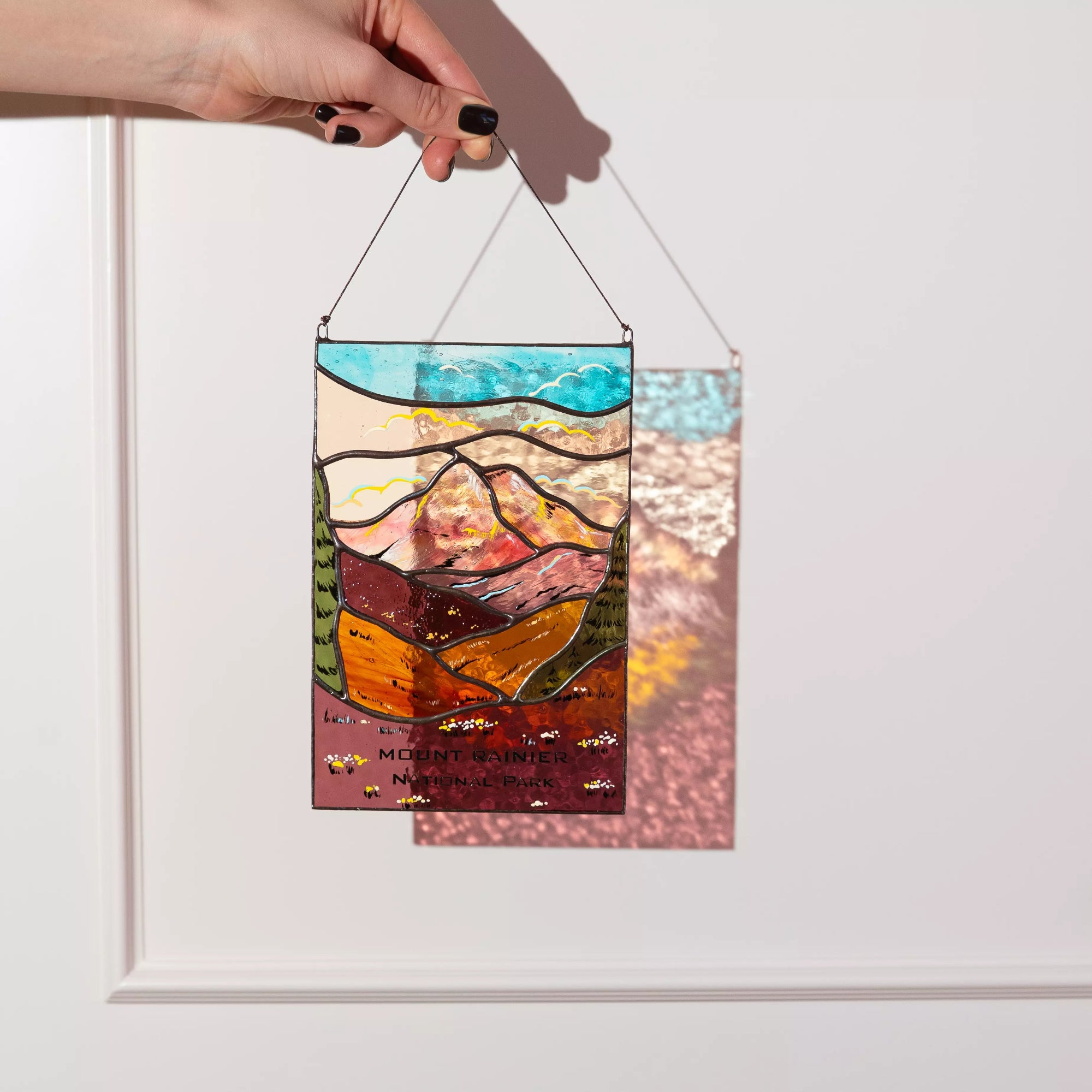 Hand holding a stained glass panel with mountain design against a white background