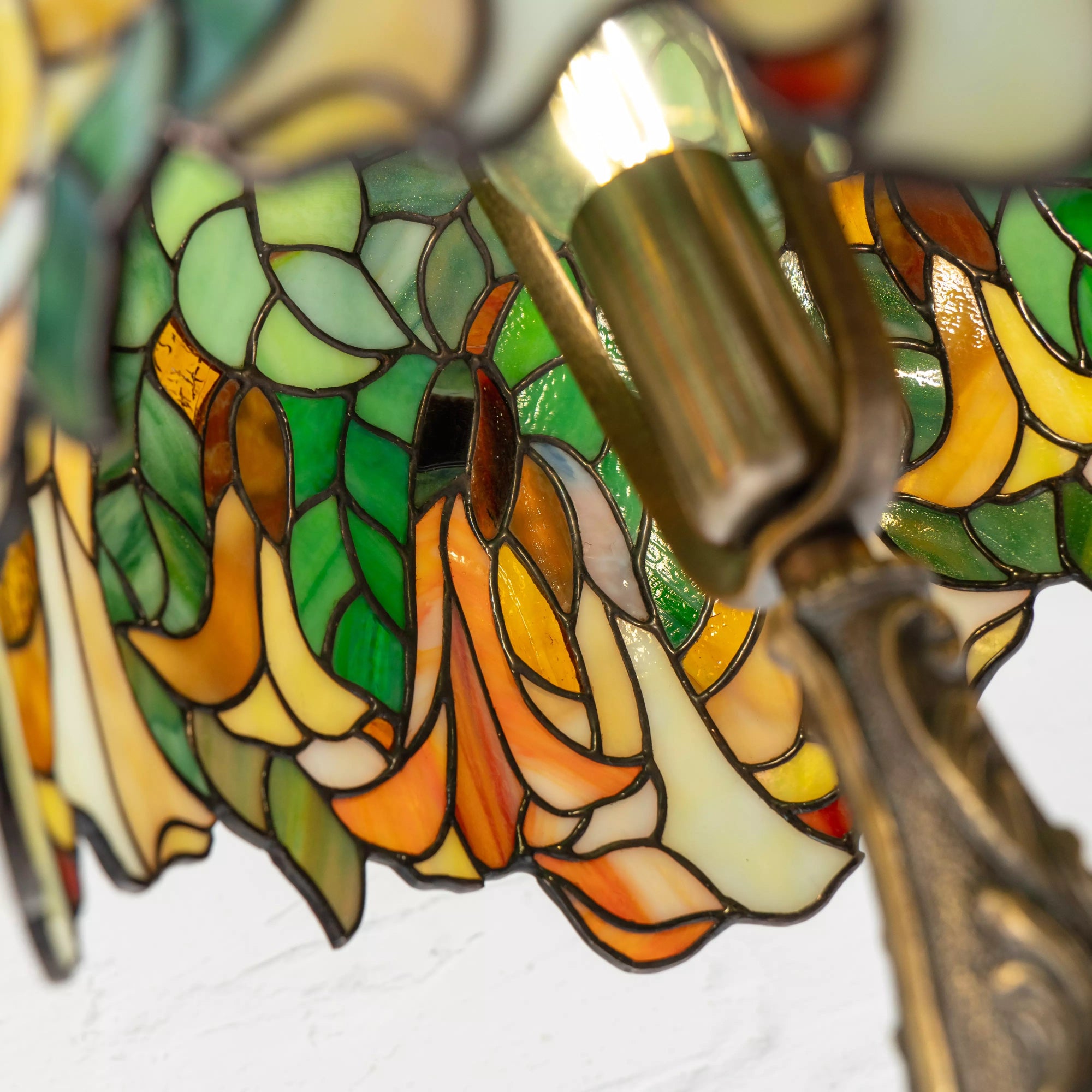 Interior view of stained glass Tiffany lamp showing warm bulb light illuminating green leaves and yellow blossoms.
