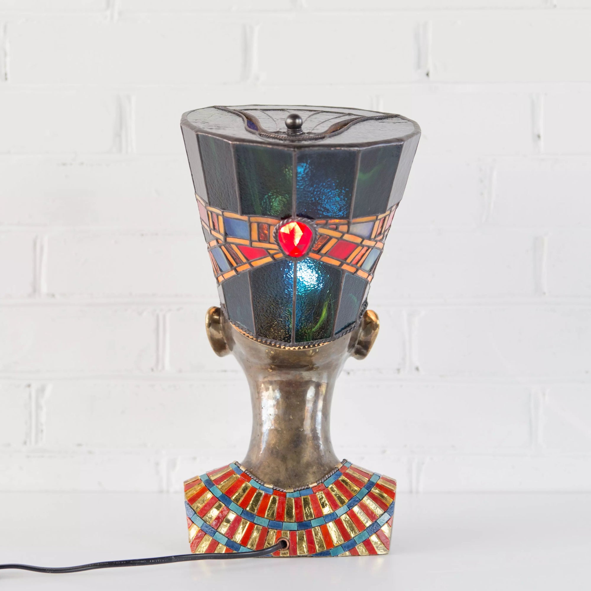 Back view of blue stained glass Nefertiti lamp on white brick background