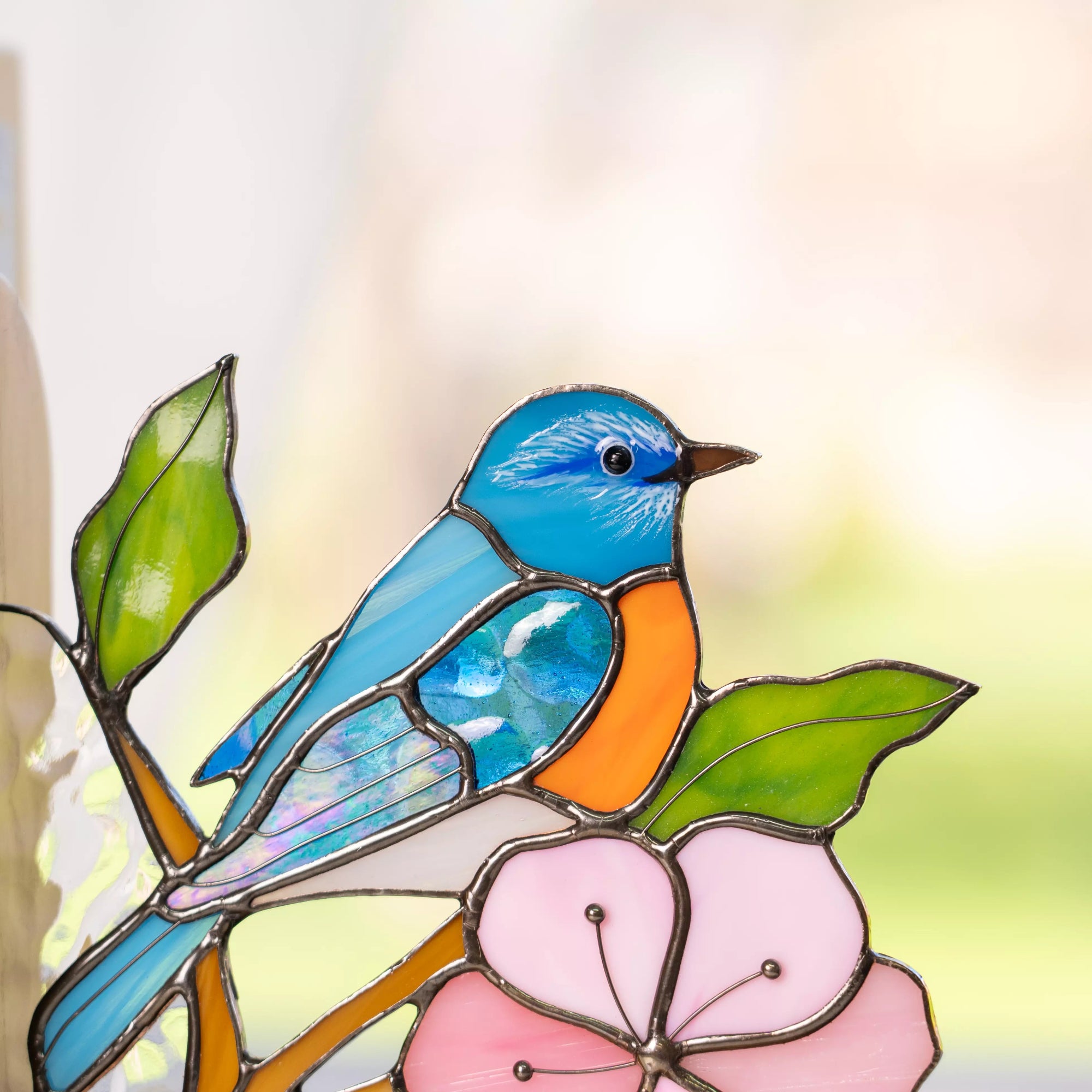 Close-up of a blue bird stained glass panel showing painted feather details, an orange chest, and a pink flower below.